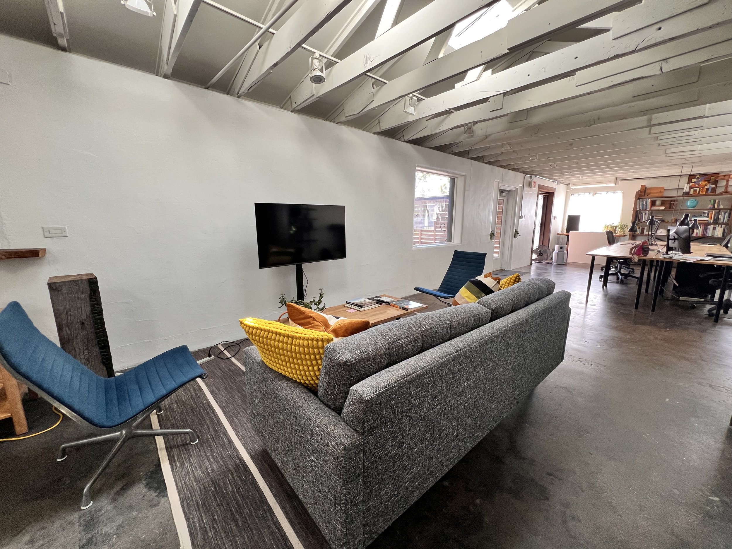 Living room with gray sofa, blue lounge chair, wooden coffee table, TV, and bookshelf. Modern decor with a high ceiling and hardwood floors.