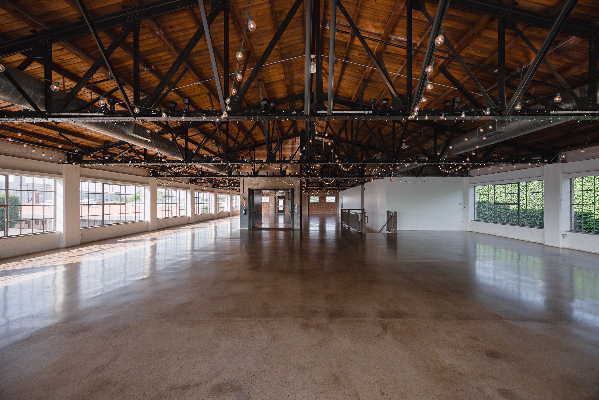 Empty spacious loft with large windows, wooden ceiling with string lights, polished concrete floor, and an open layout.