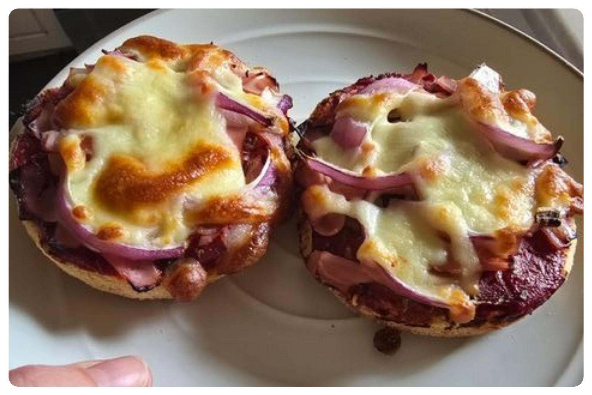 Two bagel halves topped with cheese, sliced red onions, and sliced meats on a white plate.
