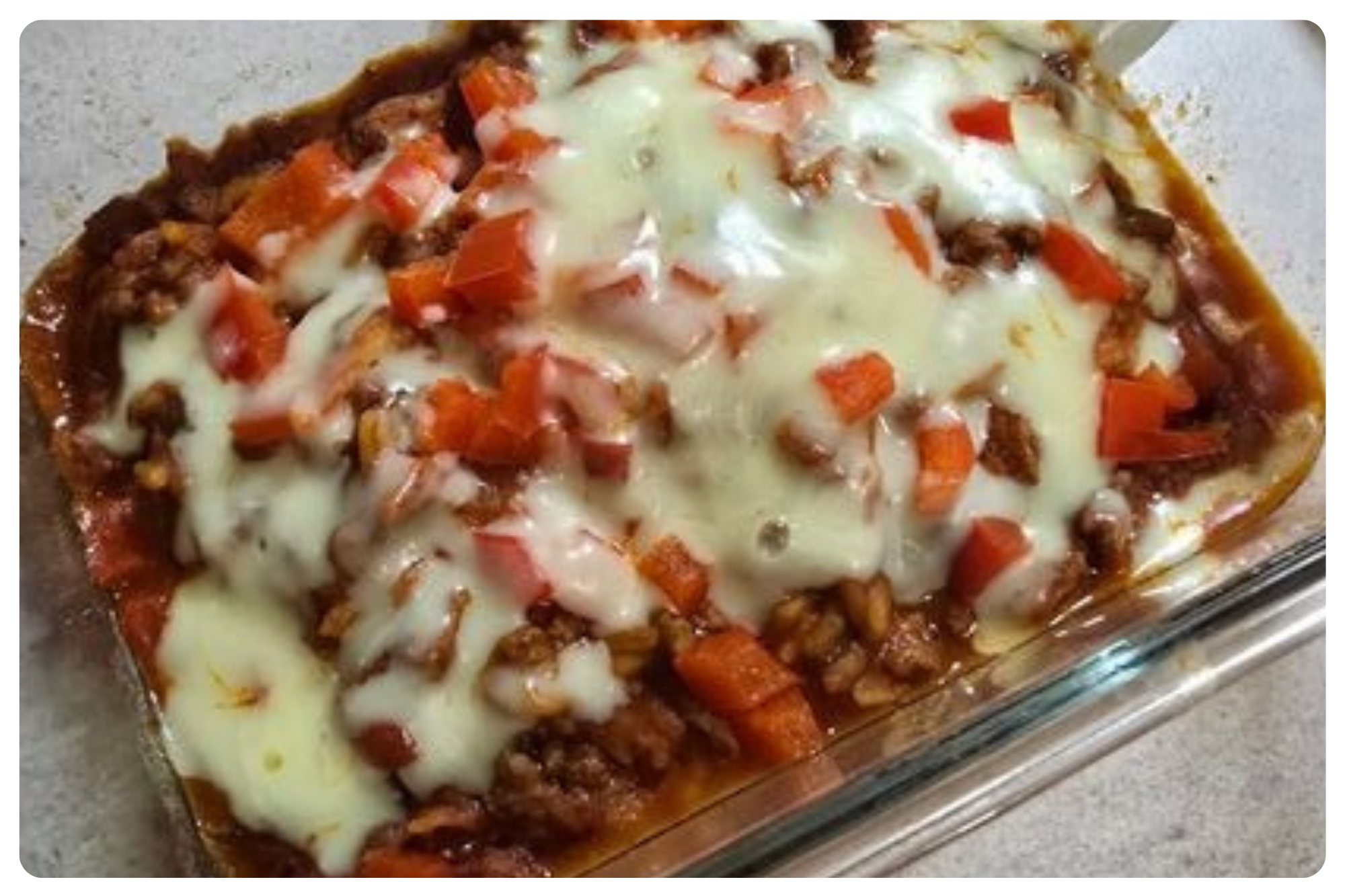 Baked lasagna with melted cheese, ground beef, chopped tomatoes, and a tomato sauce in a glass baking dish.