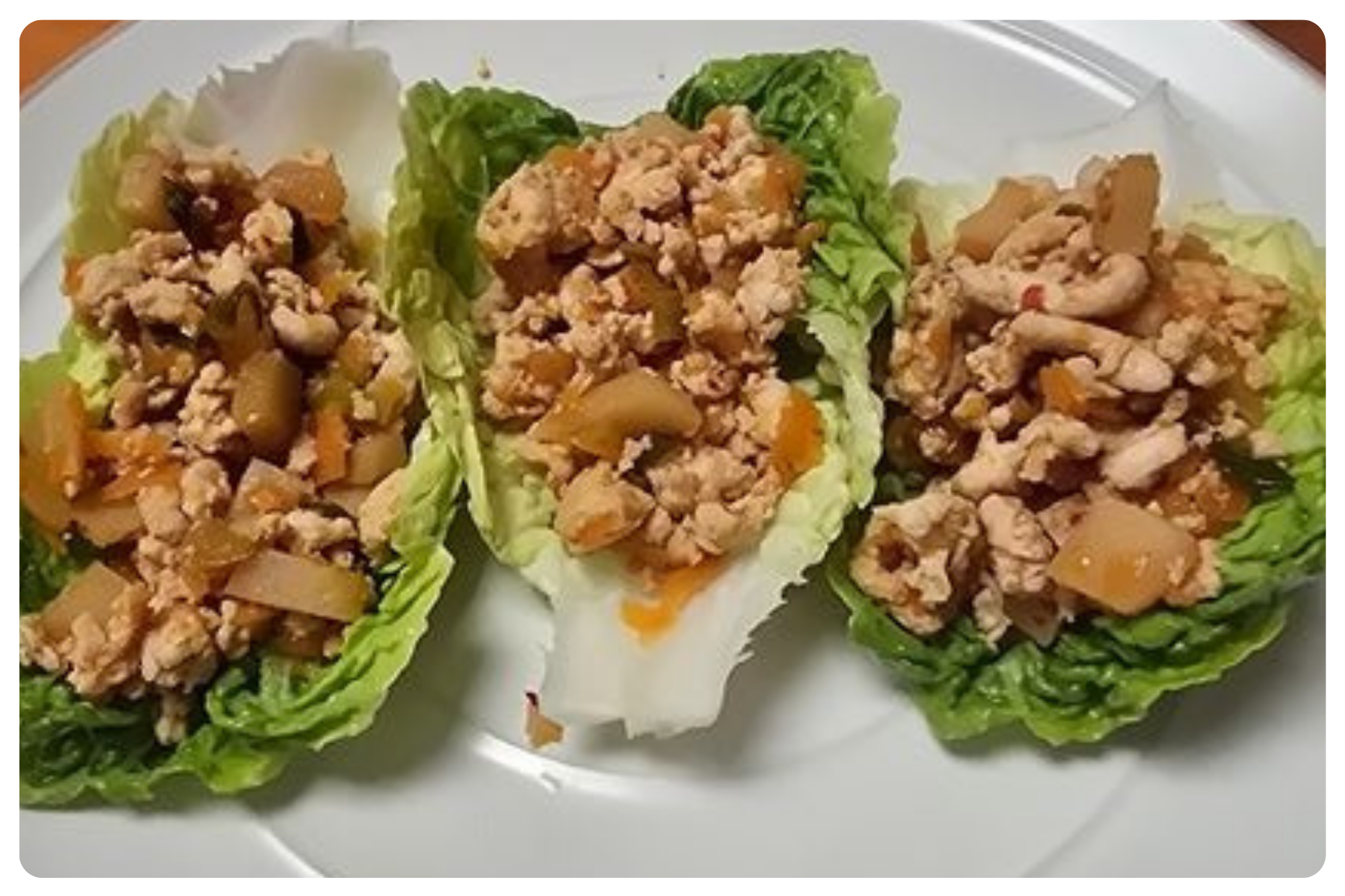 Three lettuce cups filled with cooked ground turkey, chopped vegetables, and seasonings on a white plate.