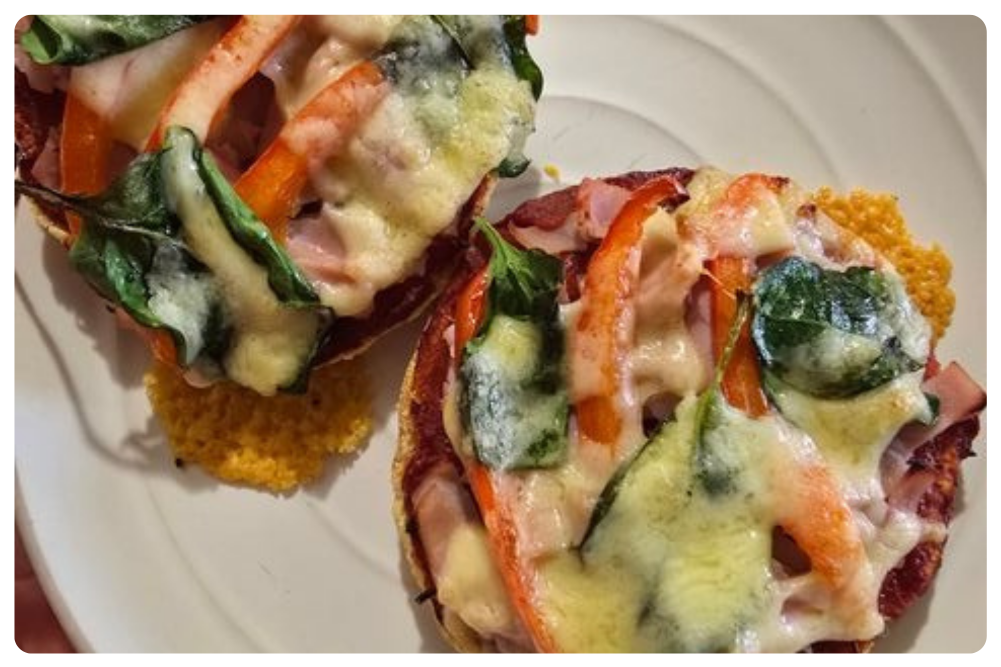Two mini pizzas with cheese, vegetables, and ham, served on a white plate with a side of fried food.