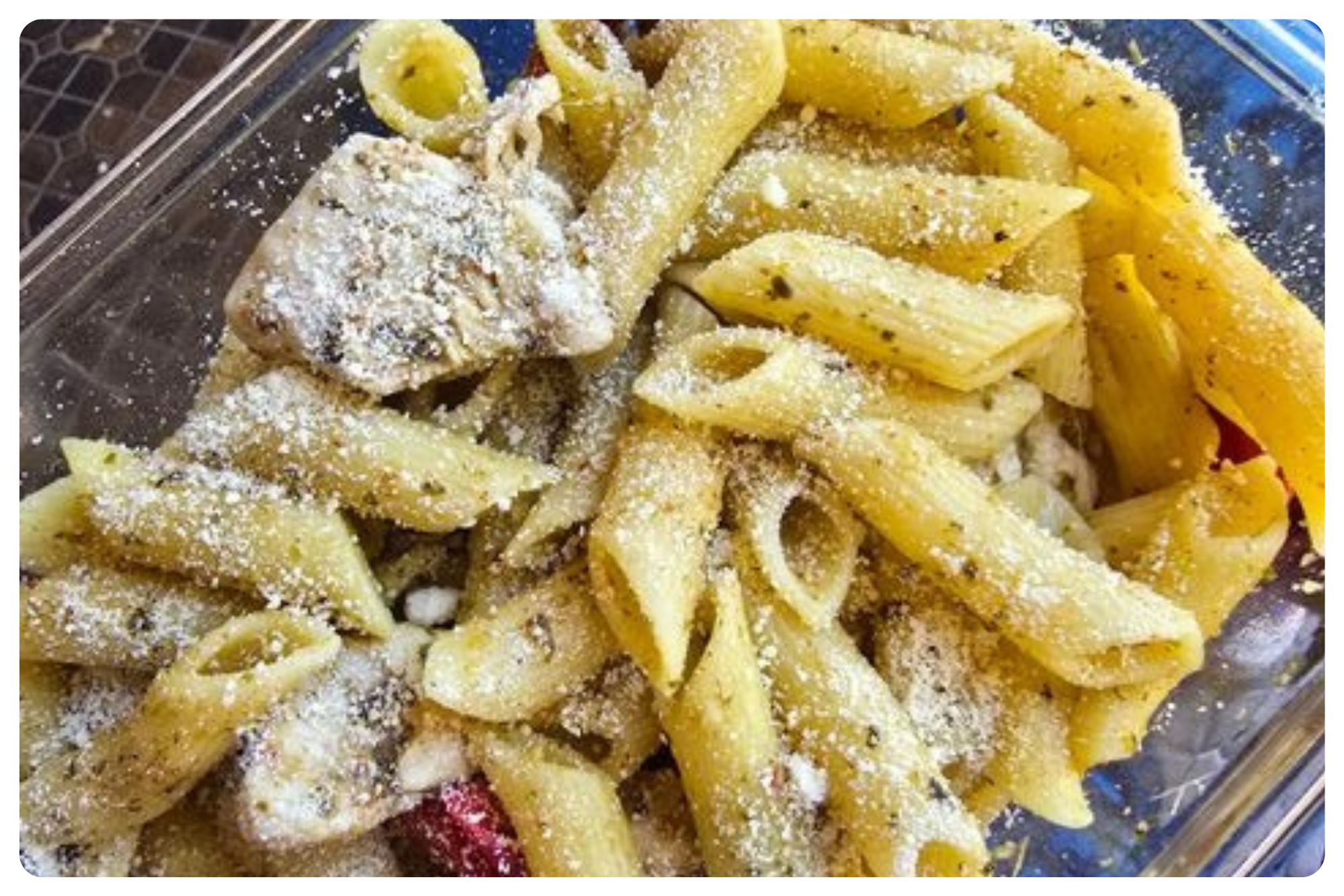 Pasta salad with macaroni, penne, and fusilli, topped with grated cheese and mixed with chicken and sliced cherry tomatoes.