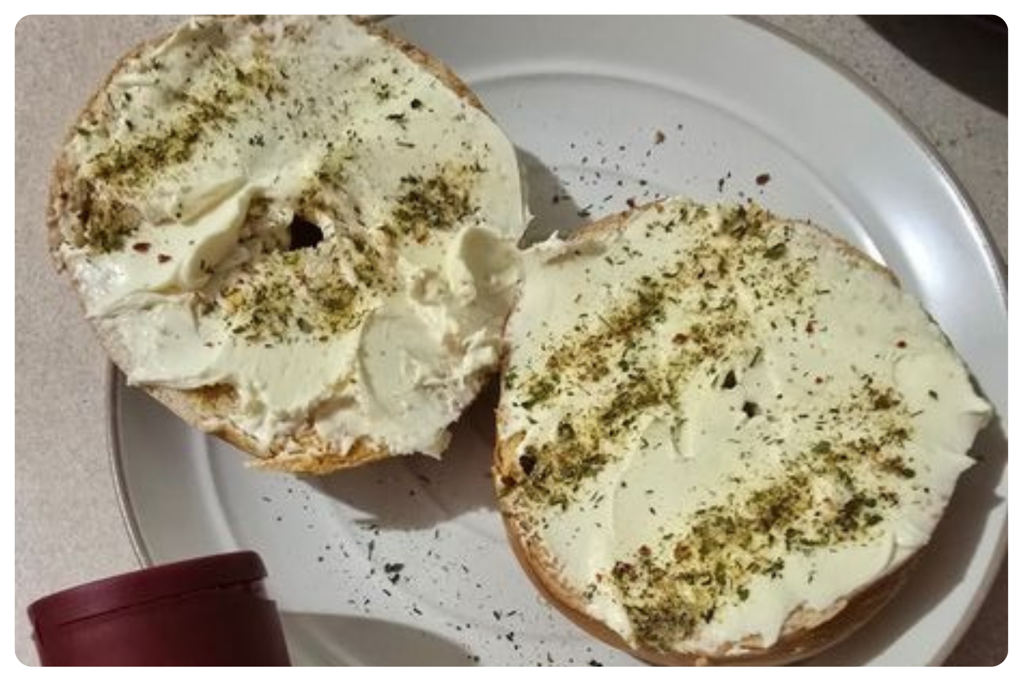 Two halves of bagel with cream cheese and herbs on a white plate.