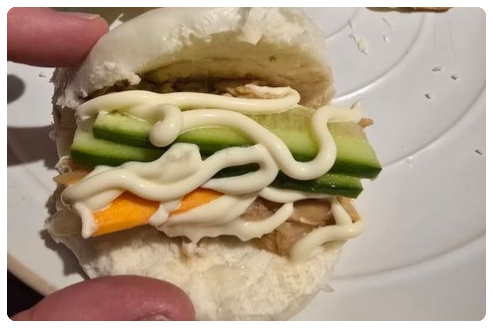 Unassembled sandwich with cucumber, carrot, mayonnaise, and chicken on a steamed bun.