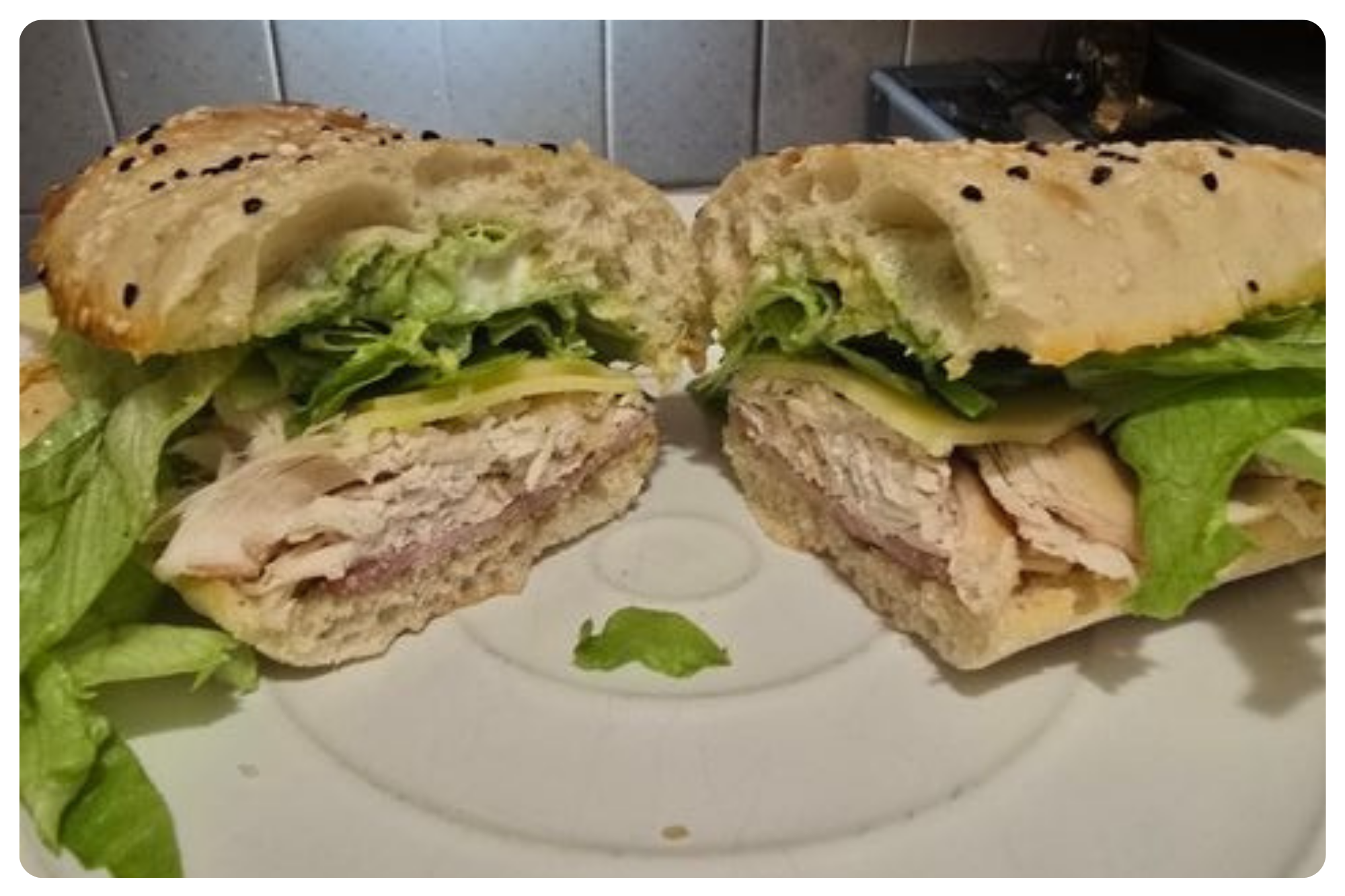 A cut sandwich with lettuce, turkey, cheese, and bun, split into two halves on a white plate, showng the sandwich's layers.
