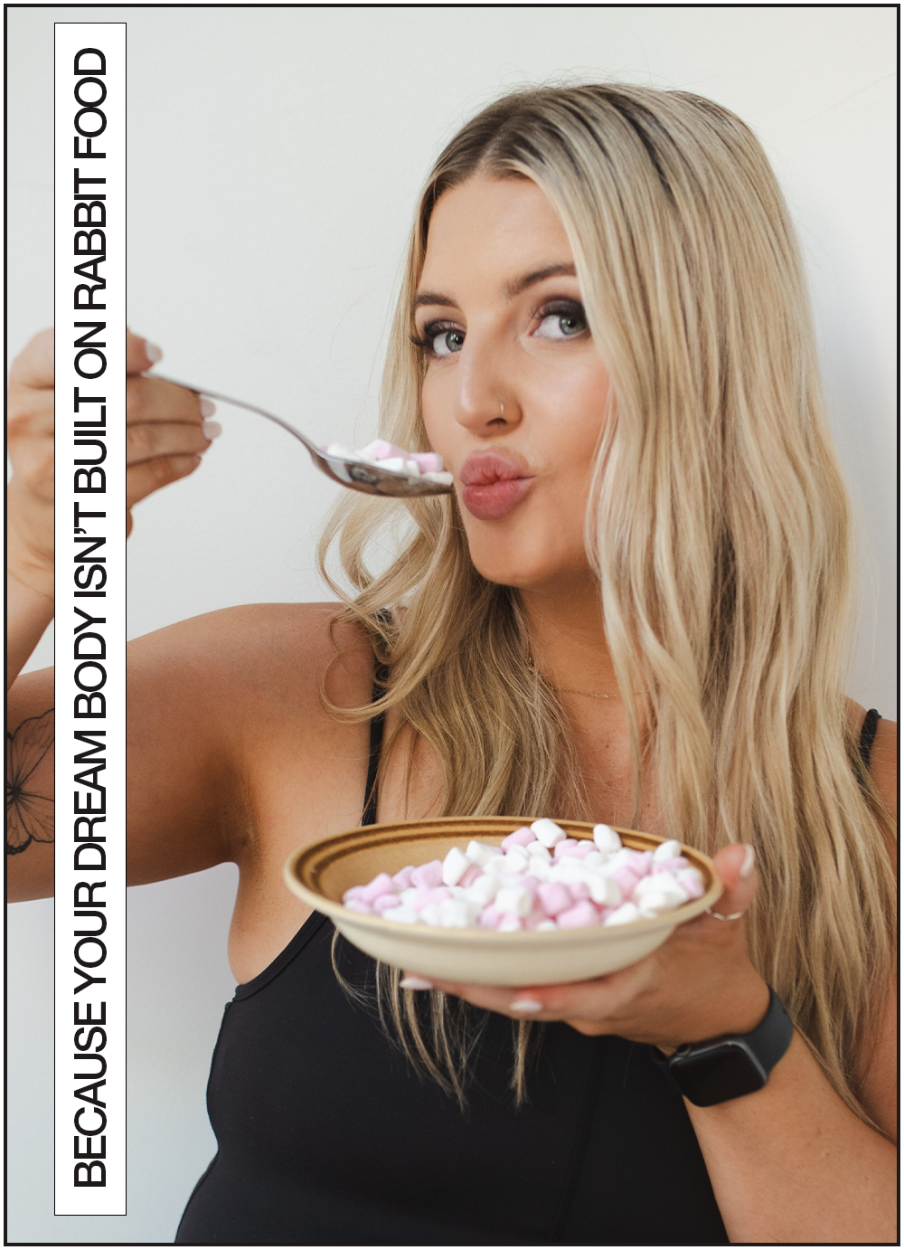 Jess Morgan, wearing a black top, is holding a bowl of pink and white marshmallows and a spoonful of marshmallows near her mouth, with a playful expression.