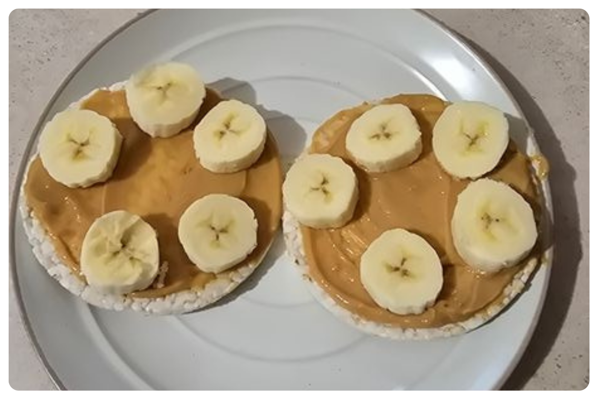 Two rice cakes topped with peanut butter and banana slices on a white plate.