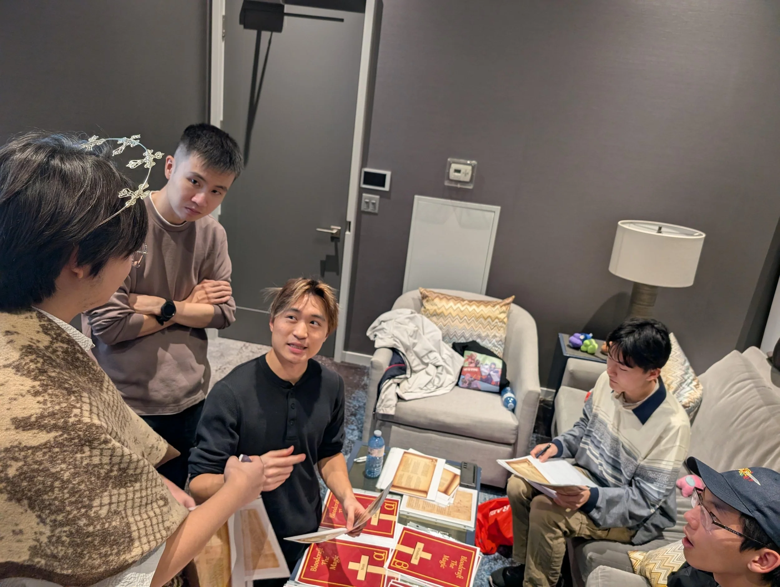 Group of five men in a cozy living room, engaged in a casual conversation, with books and magazines on the table, and a sofa and armchair with decorative pillows.