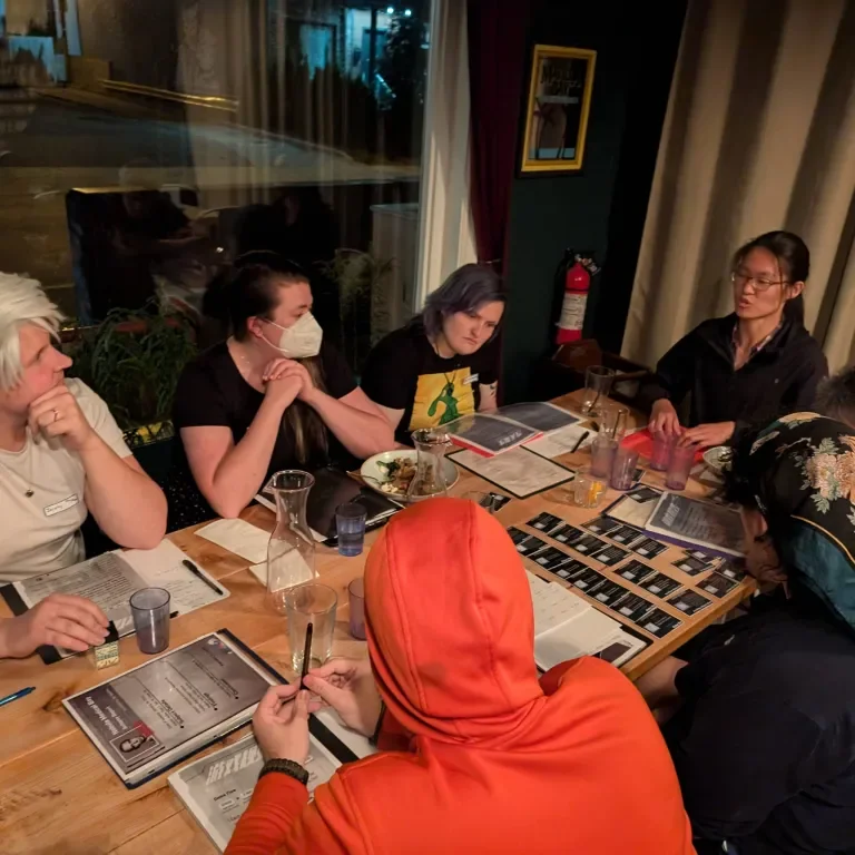 Group of people sitting around a table at a restaurant, engaged in a game or discussion.