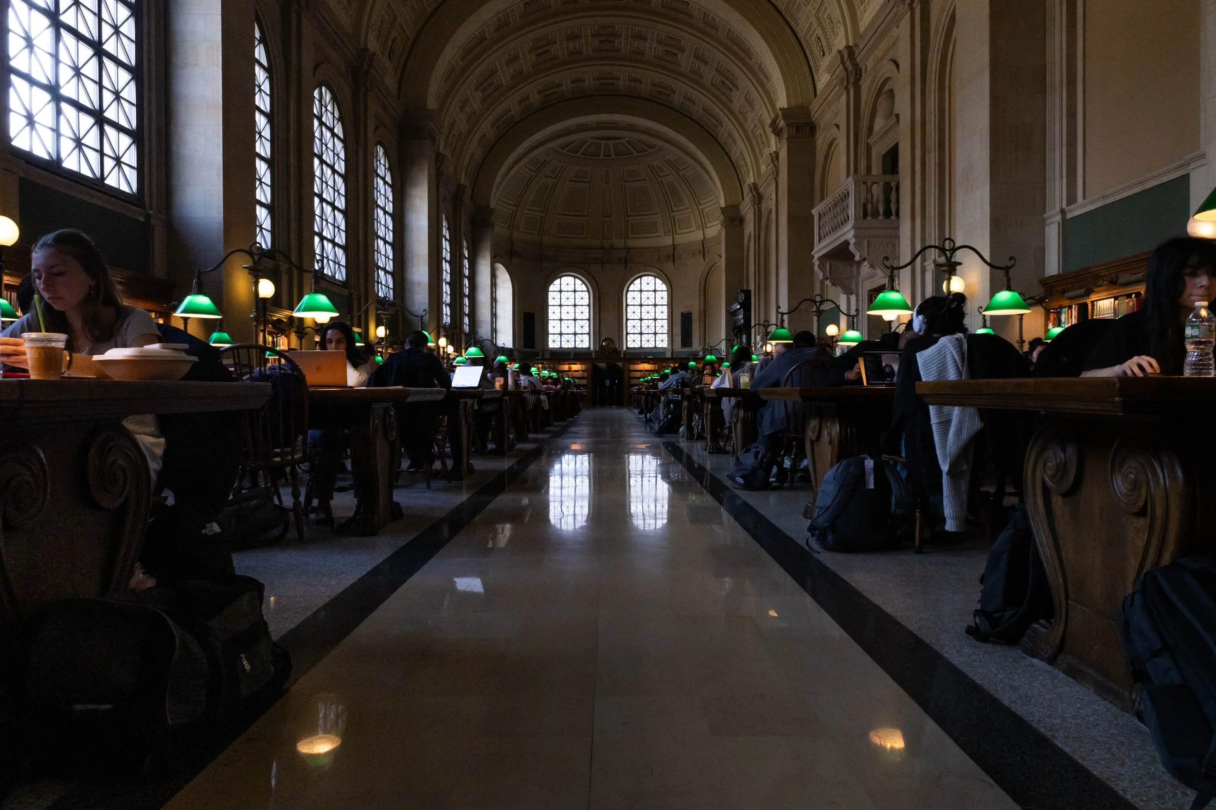Under the Lamplight  𖦹  On the second floor of the Boston Public Library, college students fill the numerous study tables lining the study hall. The library is known for its architecture and extensive special collections.