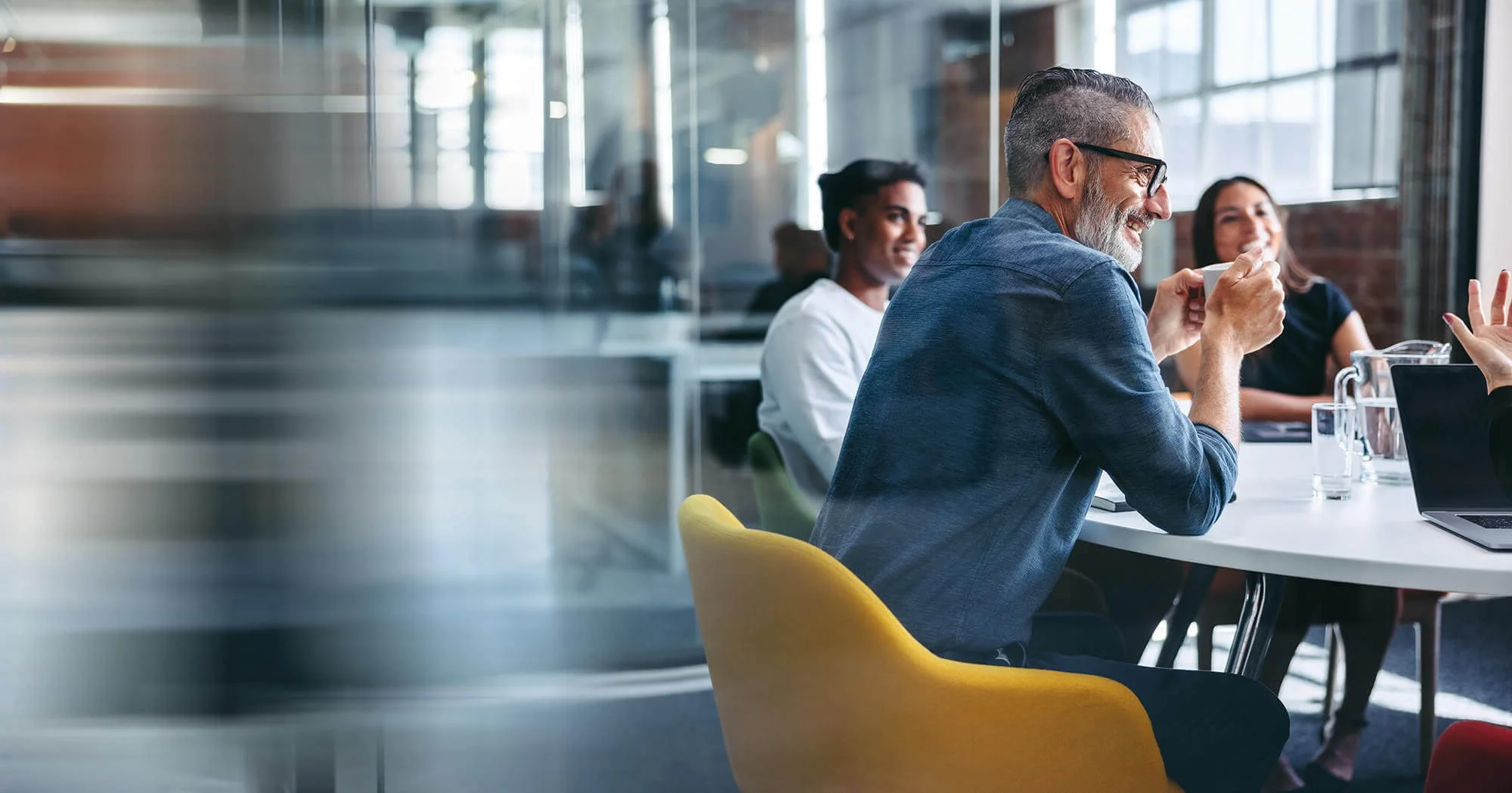A group of diverse adults sitting around a table in a modern office, engaging in conversation about innovationa nd how to use AI.