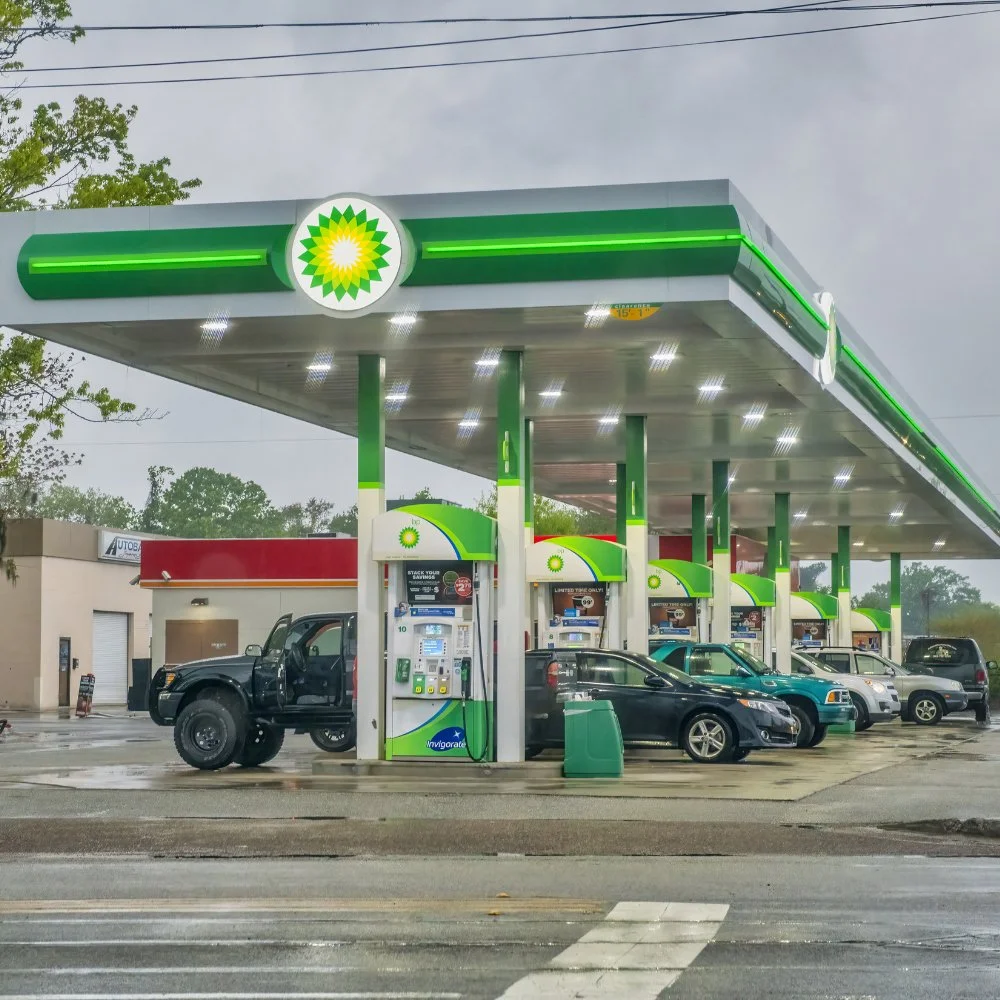 A BP gas station with multiple fuel pumps and several parked cars on a rainy day.