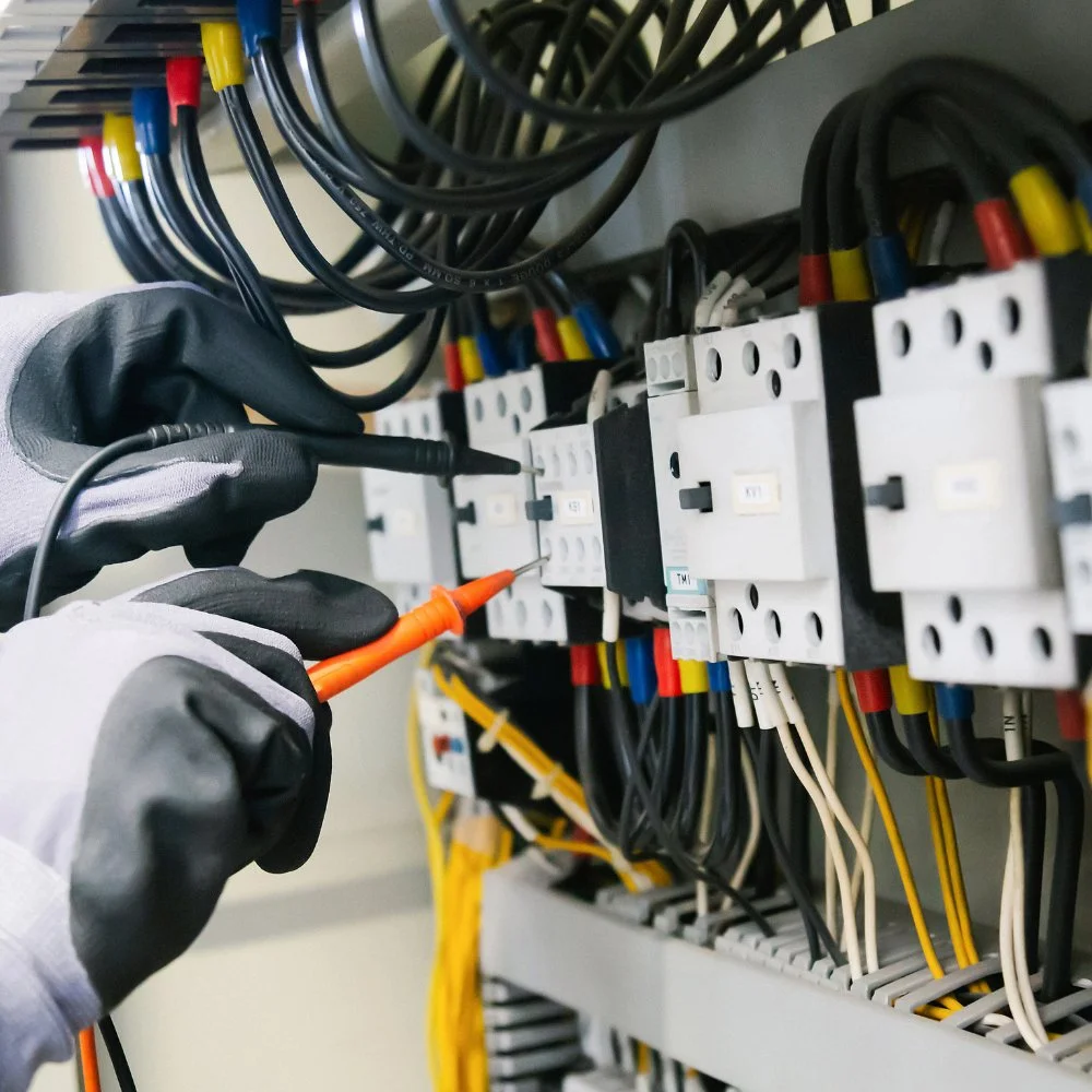 Electrician working on wiring in an electrical panel, using a screwdriver and multimeter probes.
