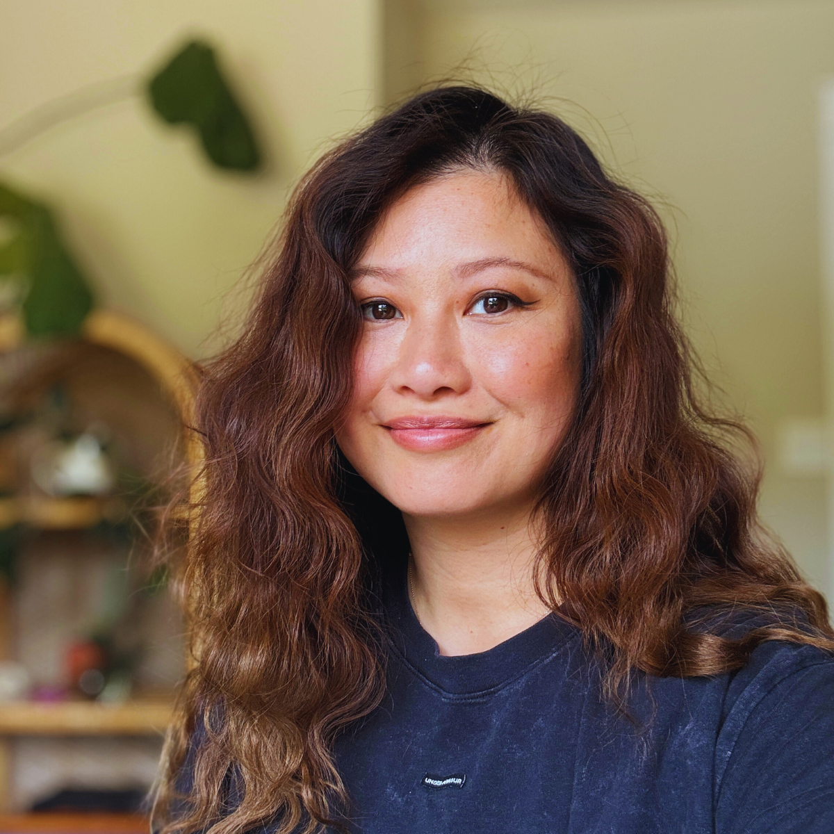 A woman with wavy brown hair smiling at the camera in an indoor setting.