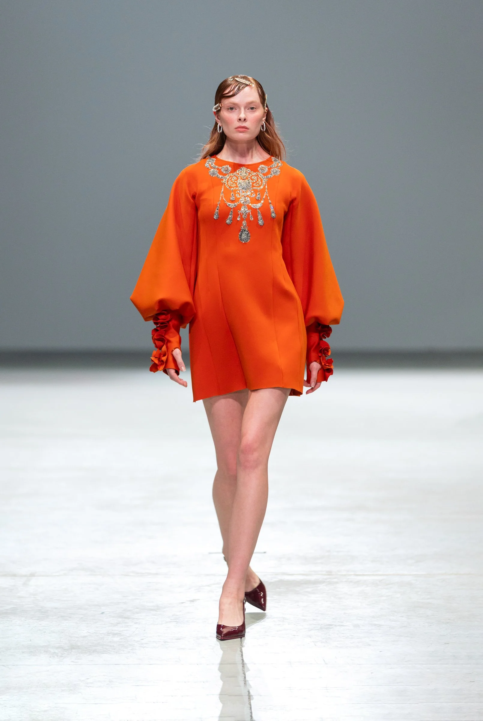  Runway moment featuring a model in a striking orange dress with long sleeves and refined tailoring from Vero Solis’ latest collection — power, femininity, and color through the KNYVAL lens. 