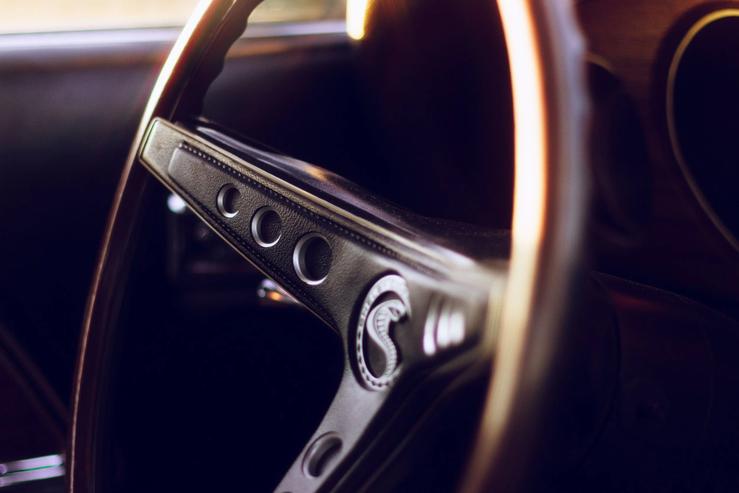 Close-up of a vintage car dashboard, showing steering wheel and controls with warm lighting.