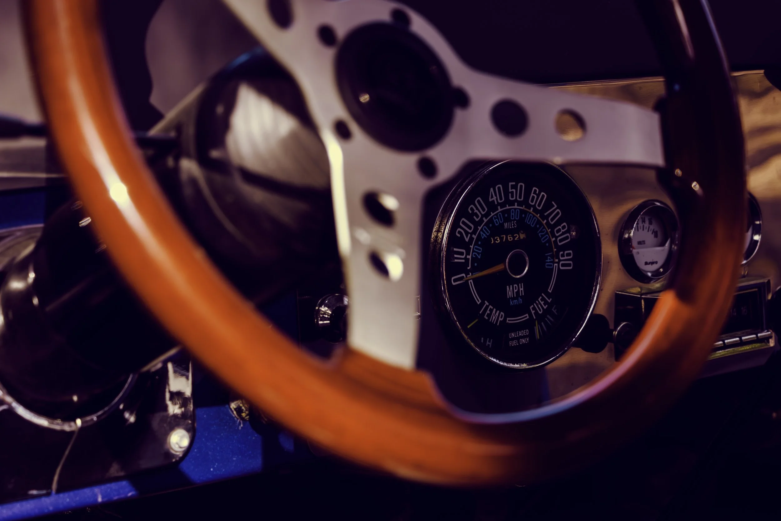 Close-up of a vintage car dashboard featuring a speedometer, odometer, and gauges with a wooden steering wheel.
