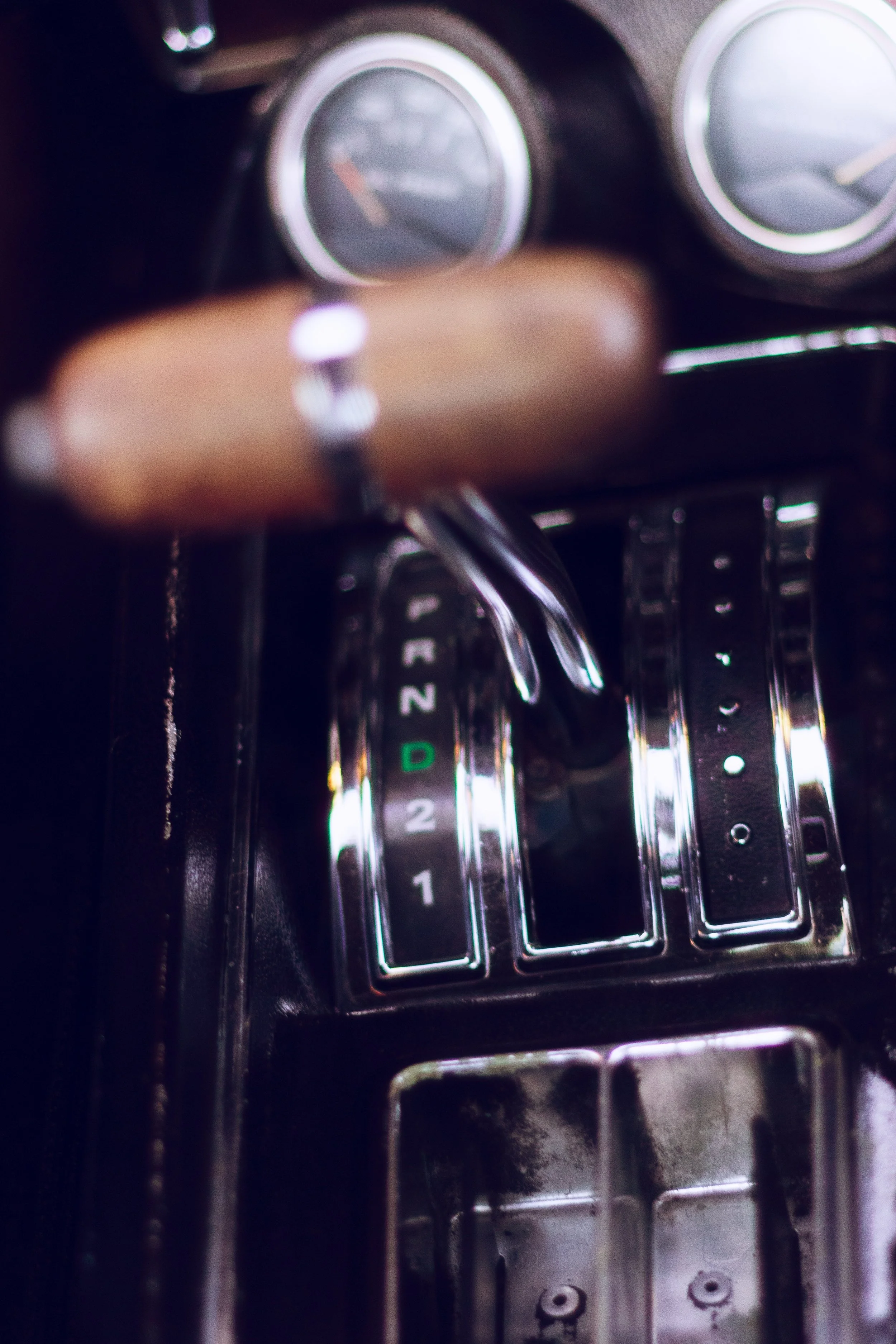 Close-up of car gear shift with the gear positions marked, including 'D' for drive, and part of the speedometer in the dashboard in the background.