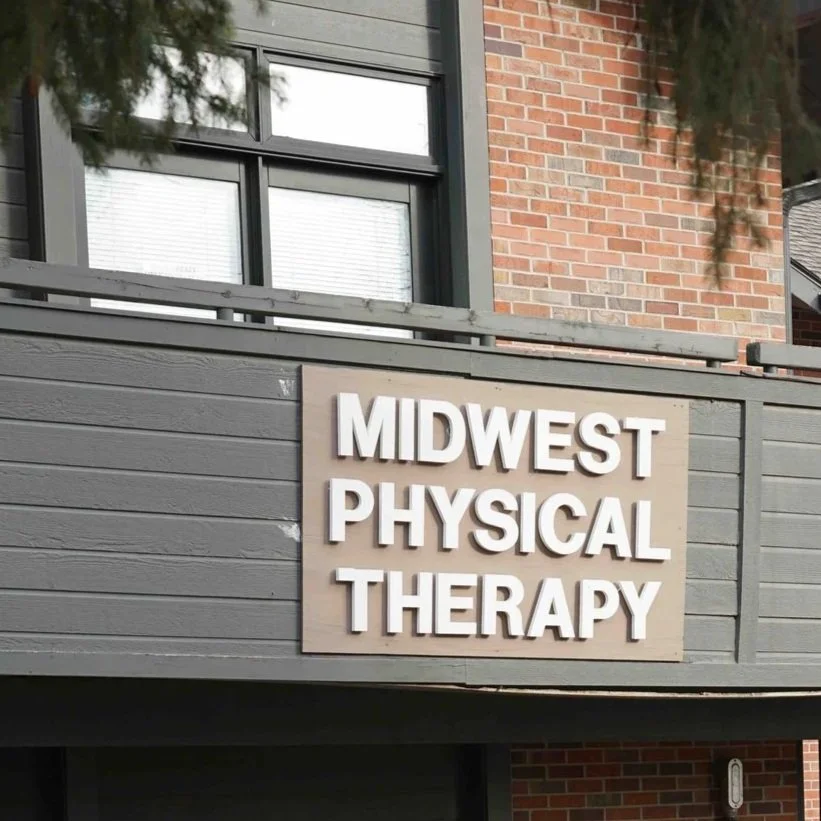 Sign for Midwest Physical Therapy on a gray wooden exterior wall of a building with a brick section above.