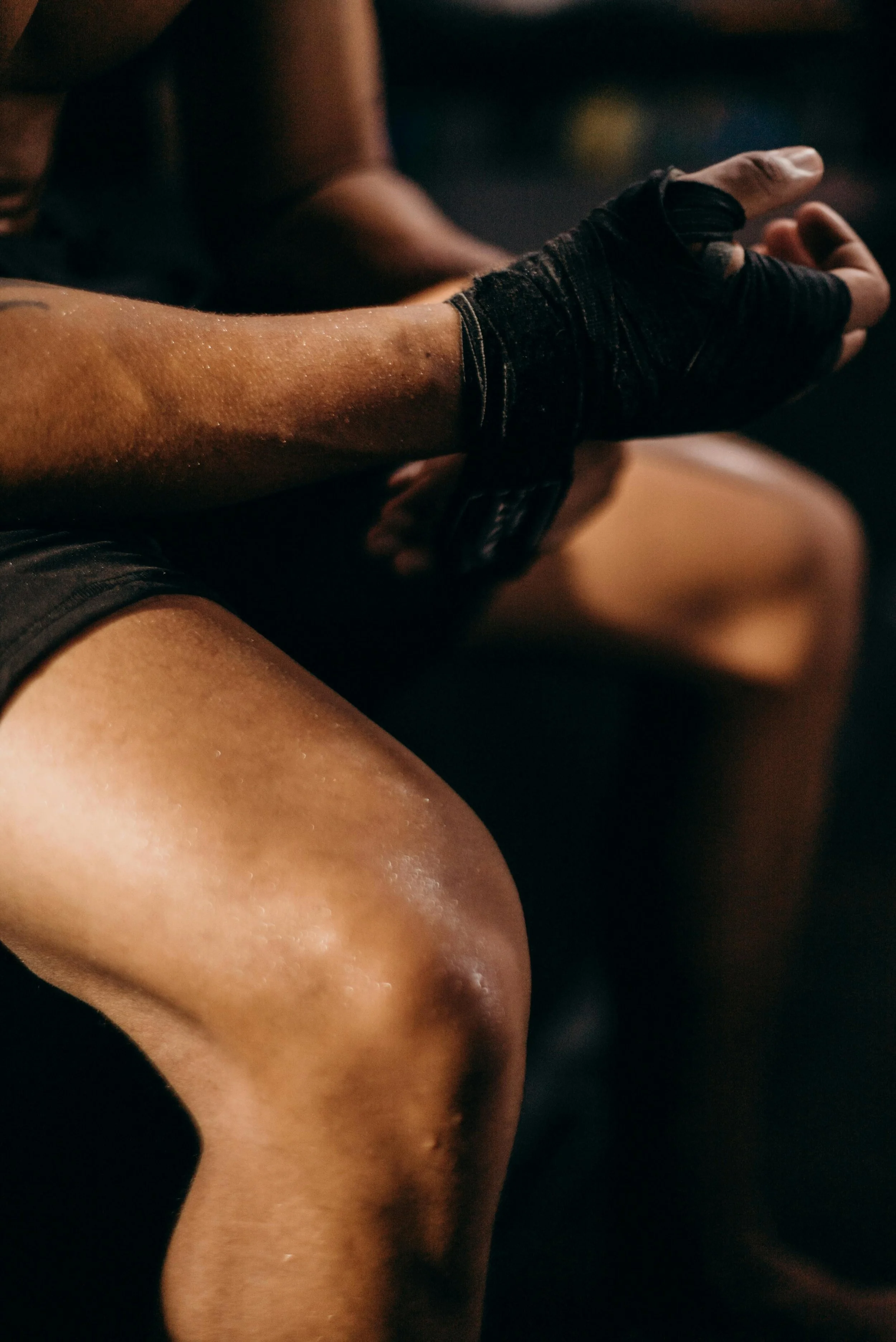 A person in workout attire with boxing hand wraps, sitting with their knee bent.