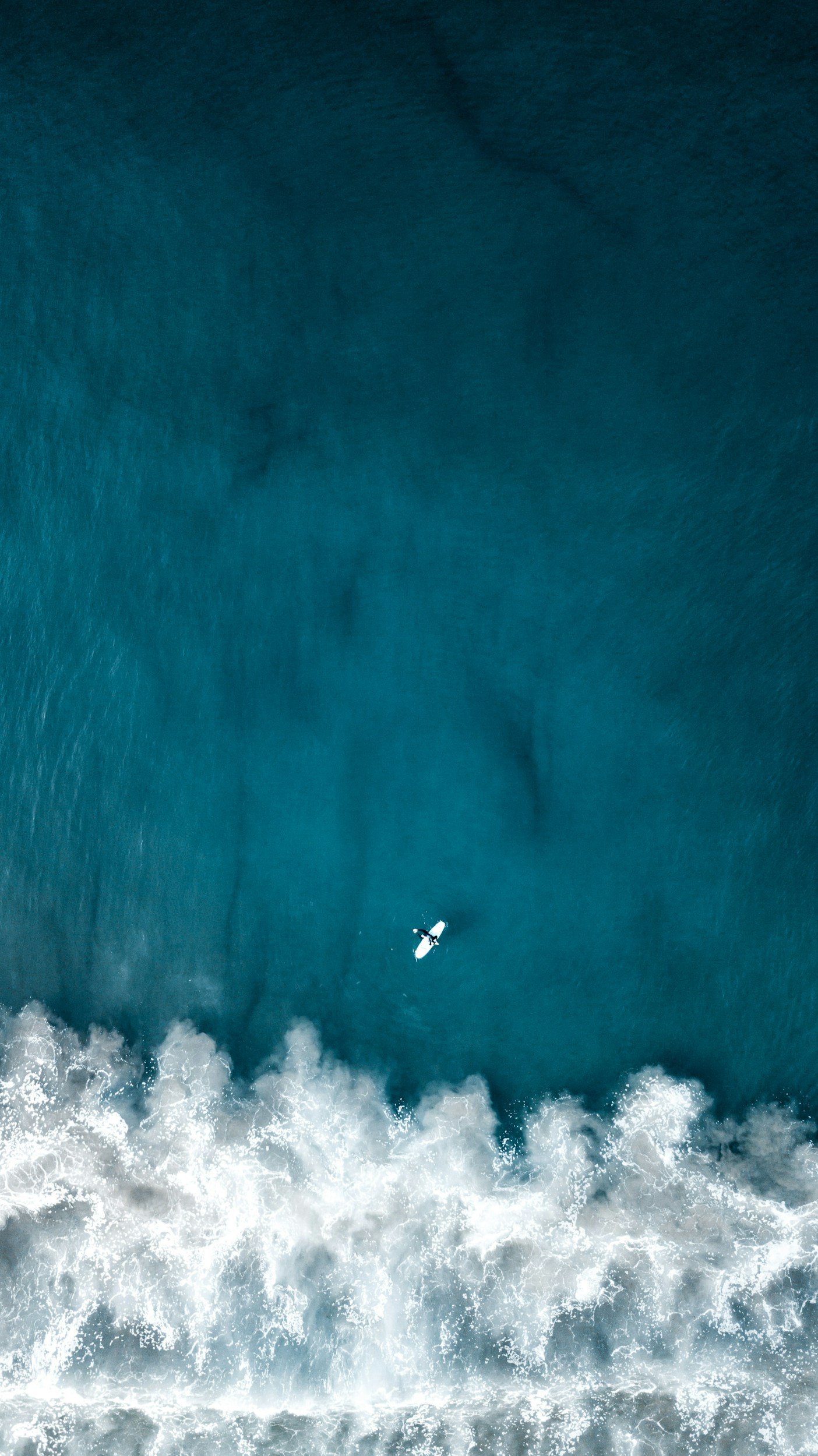 An aerial view of the ocean showing a small boat and white waves crashing at the shoreline.