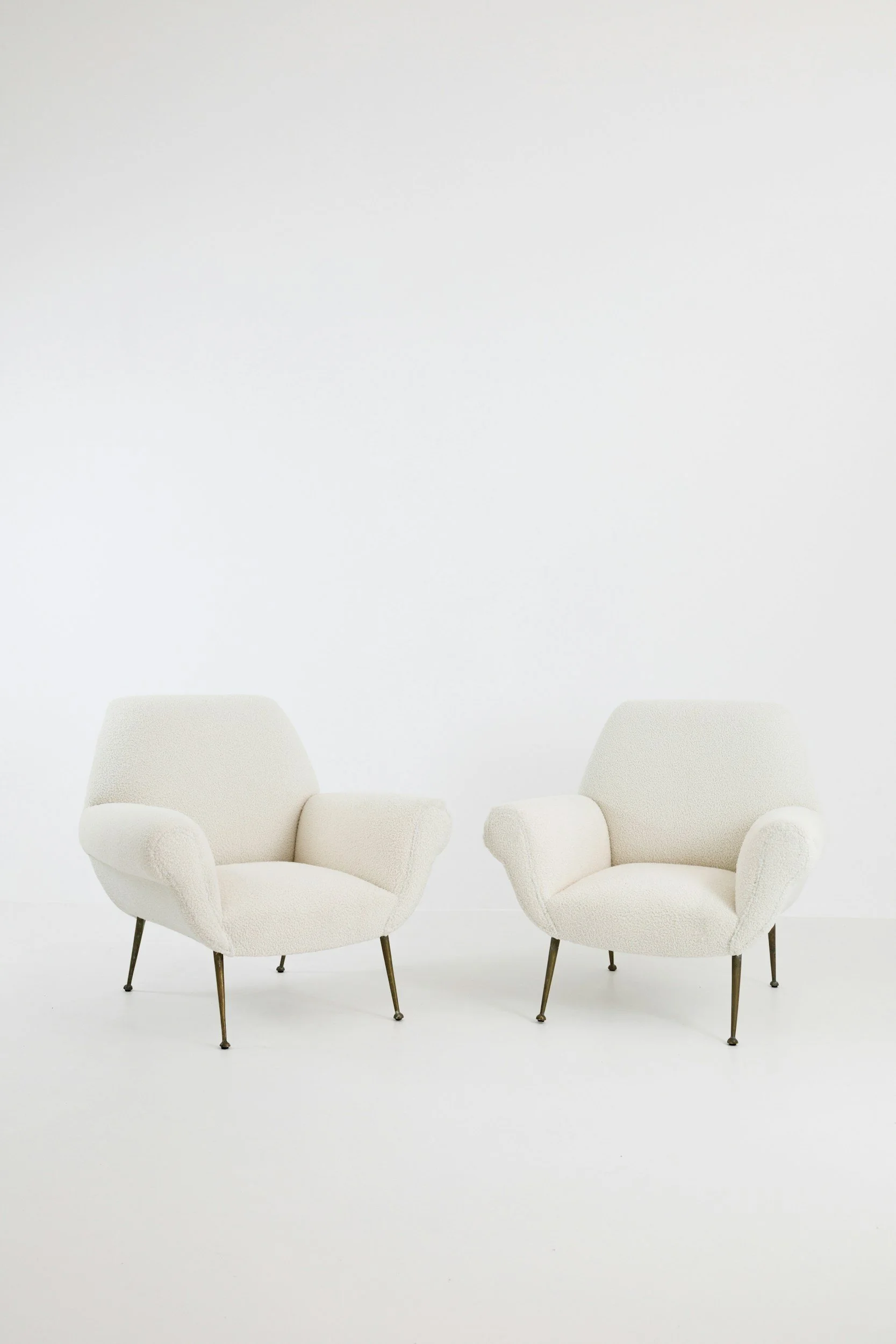 Two cream-colored armchairs with slim metallic legs are placed in a white room.