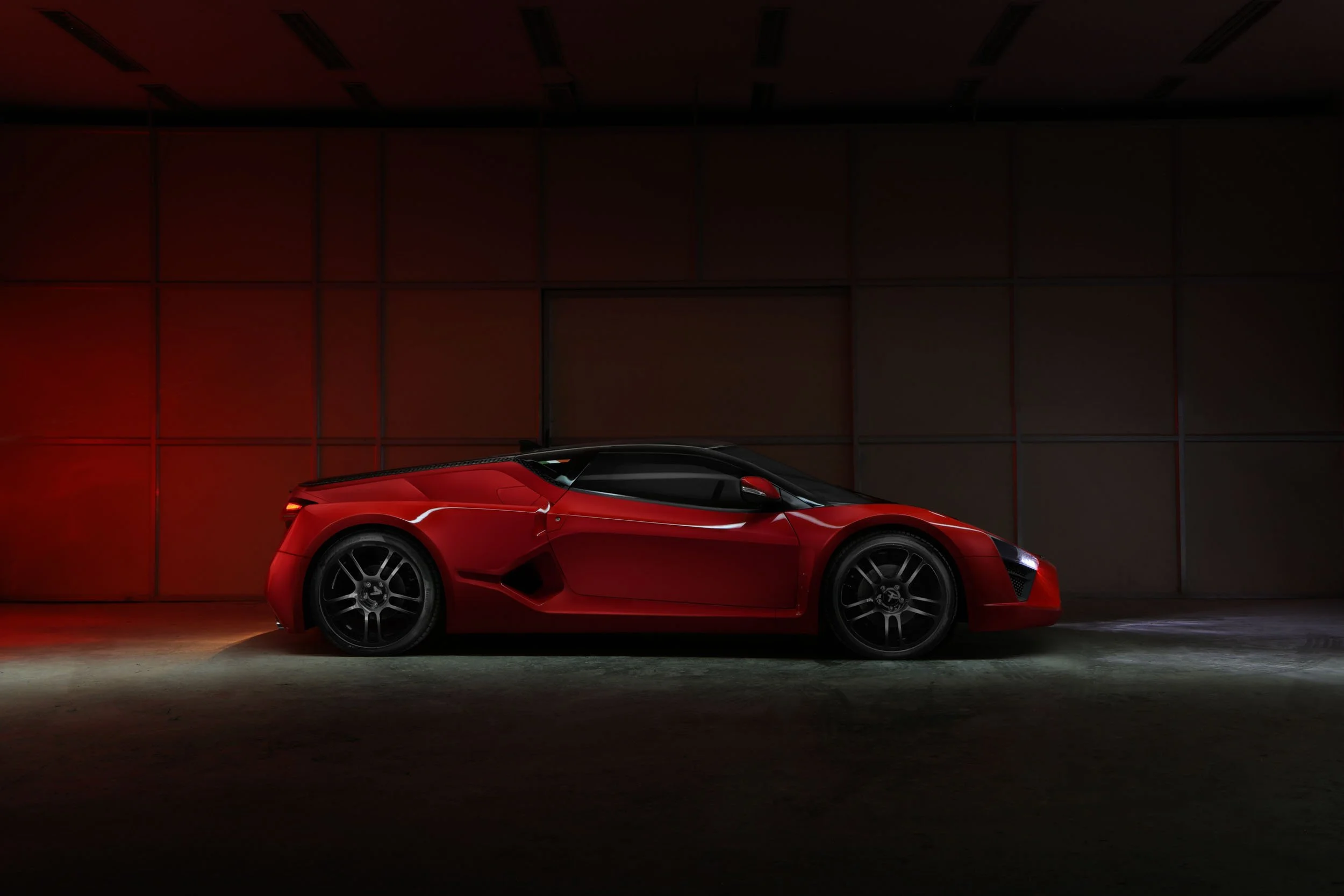 A red sports car parked against a dark wall, low lighting highlights its sleek design.