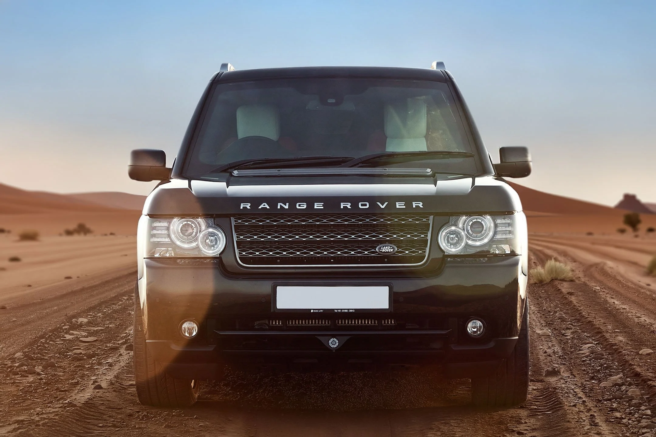 Front view of a black Range Rover SUV on a dirt road in a desert landscape during daylight.