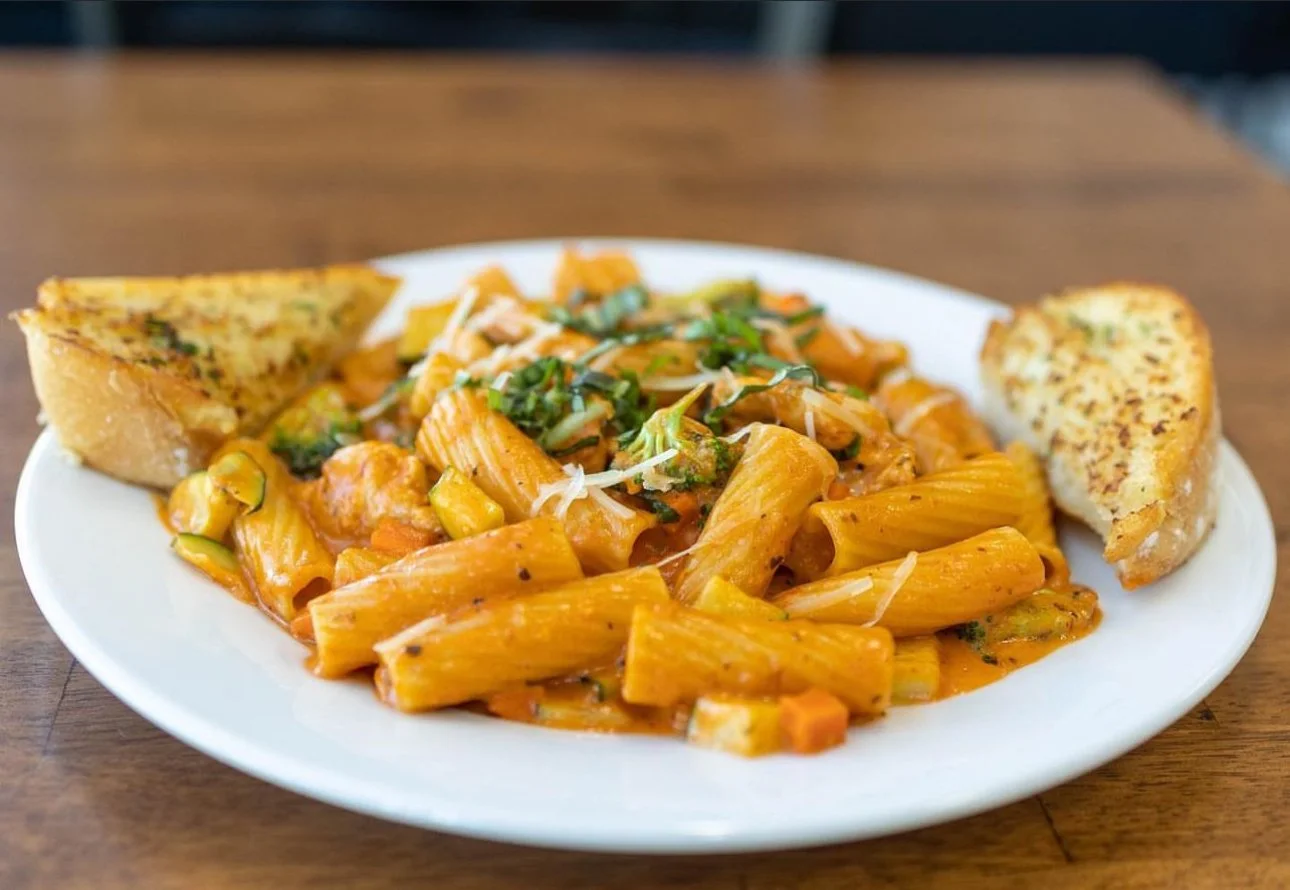 Plate of pasta with tomato sauce, garnished with basil and grated cheese, served with two pieces of garlic bread.