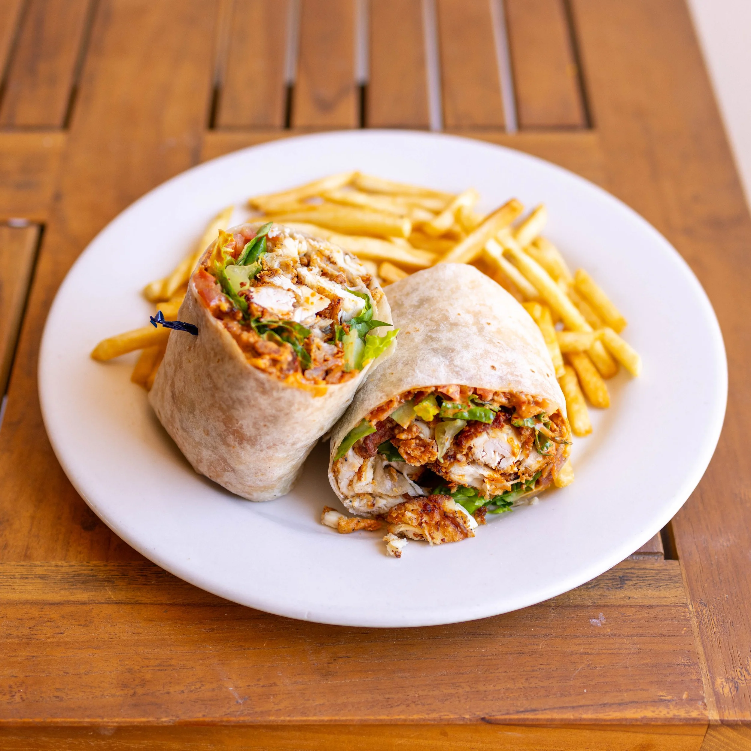 Plate with two chicken wraps and French fries on a wooden table.