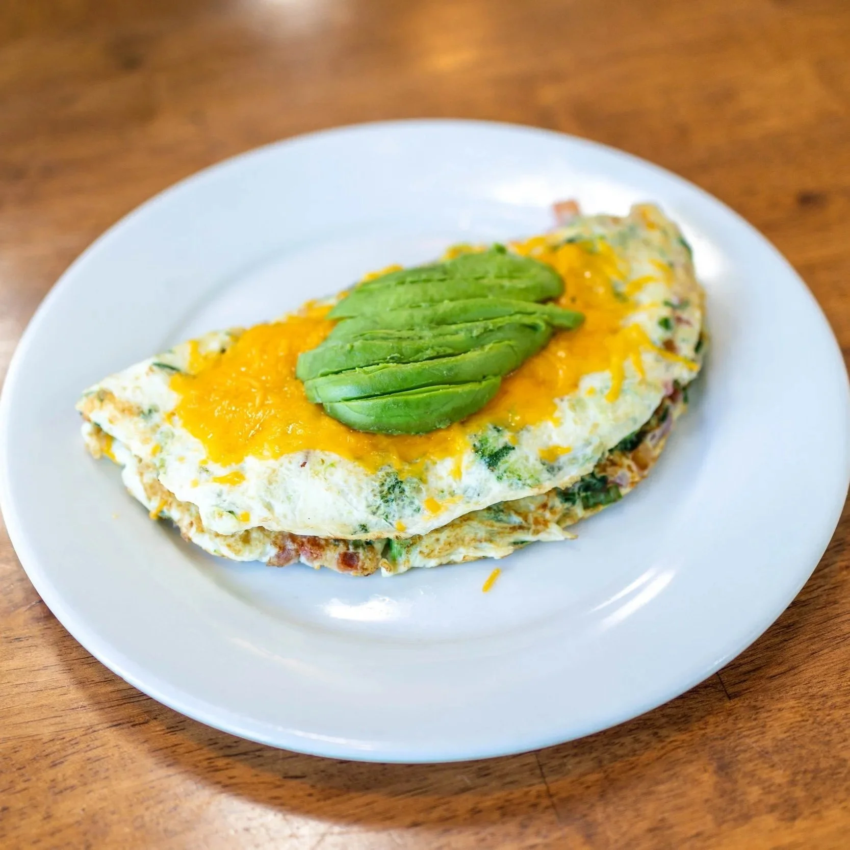 Omelette topped with sliced avocado on a white plate.