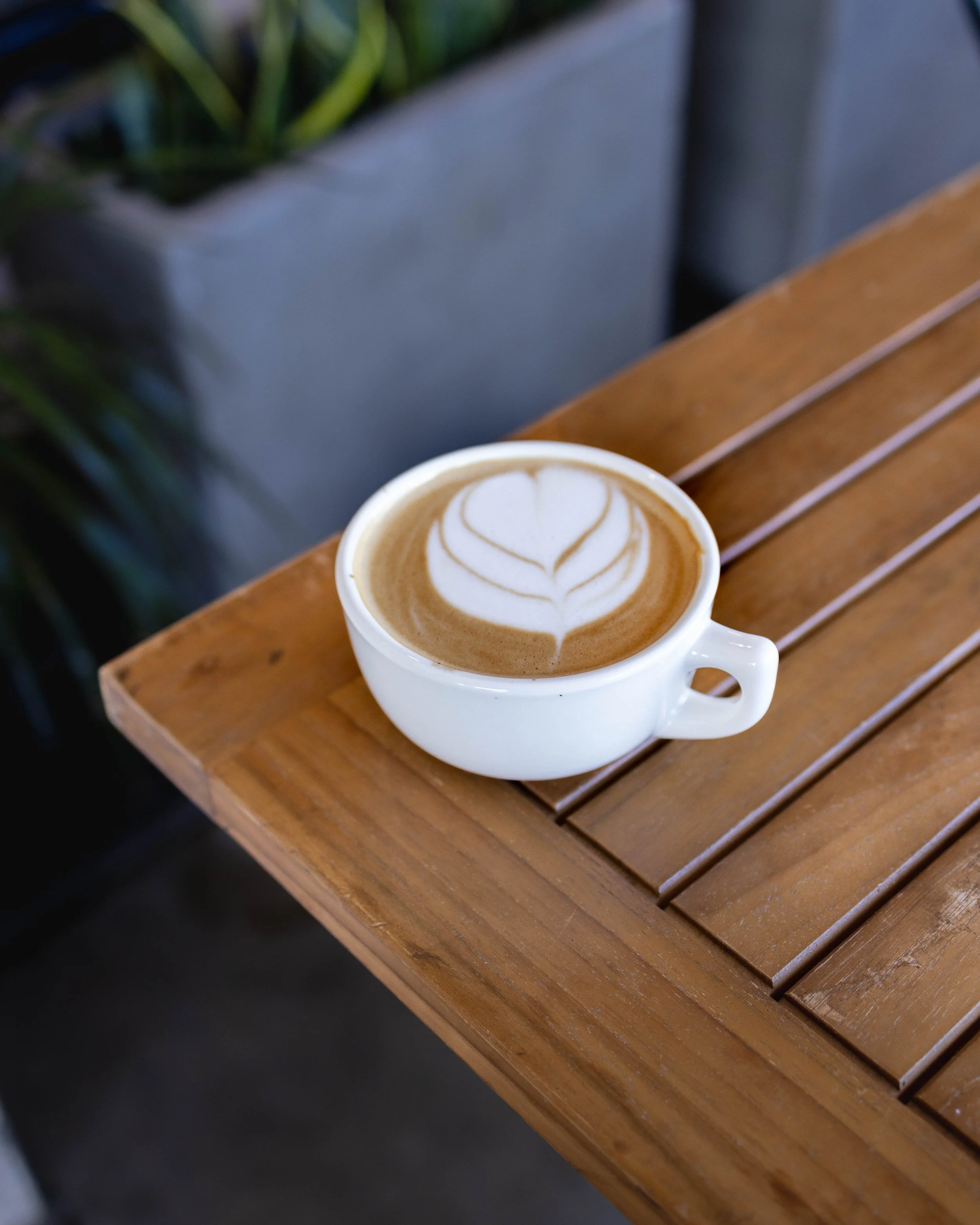 A white cup of latte with heart-shaped latte art on top, placed on a wooden table.