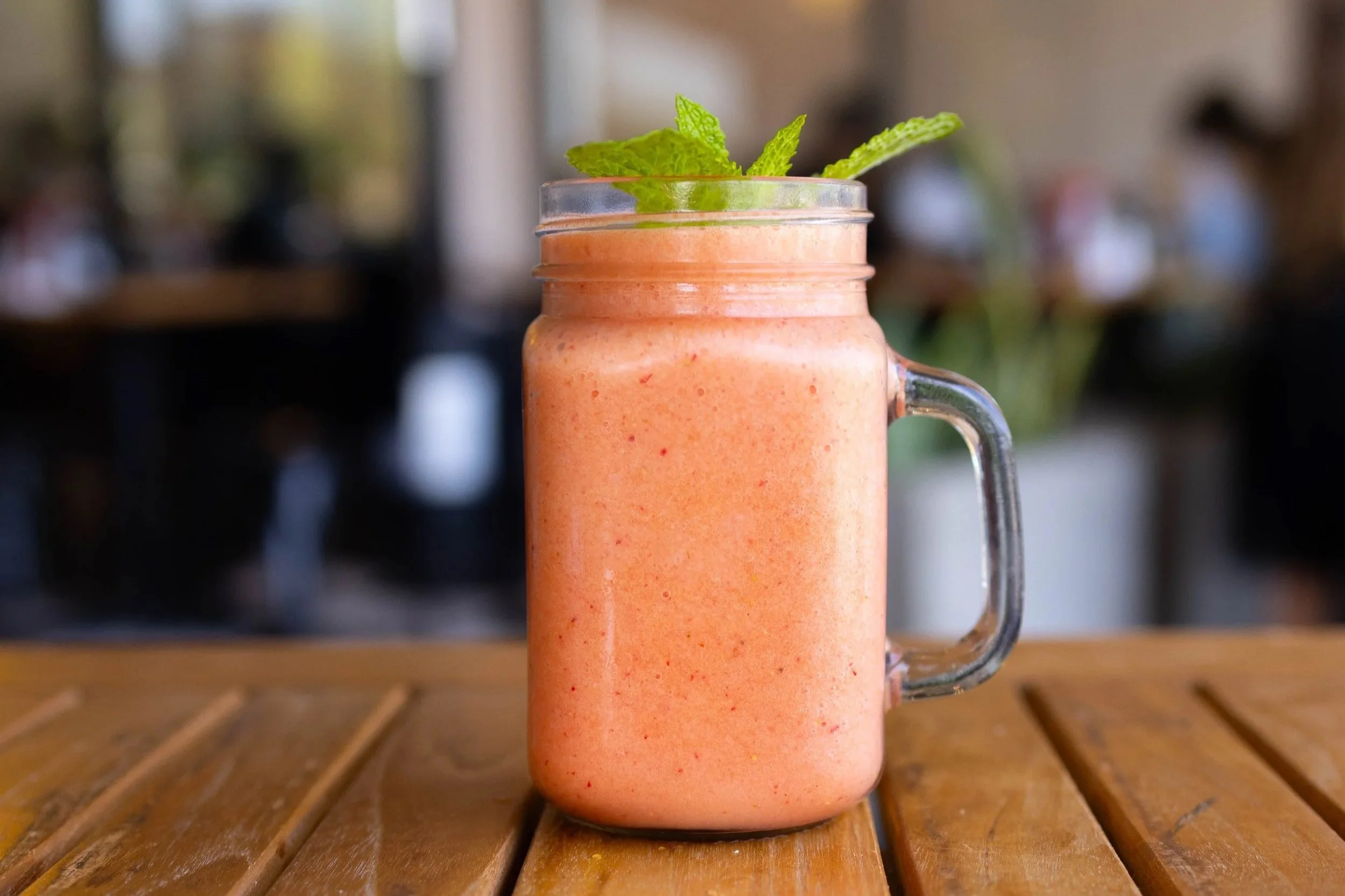 A pink smoothie in a glass jar with a handle, garnished with fresh mint leaves.