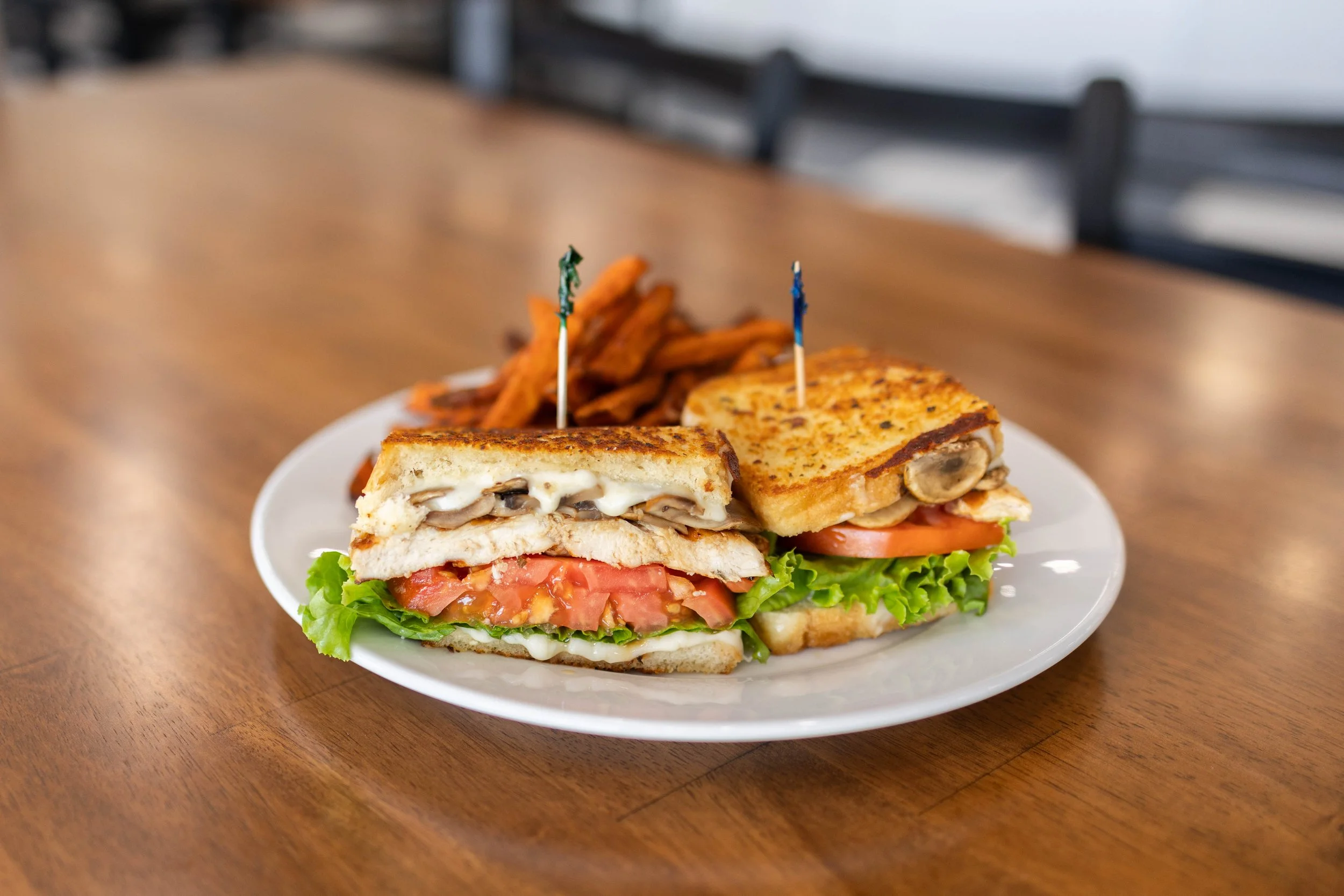 Plate with two grilled sandwiches, tomato and lettuce, French fries, and pickles on a wooden table.