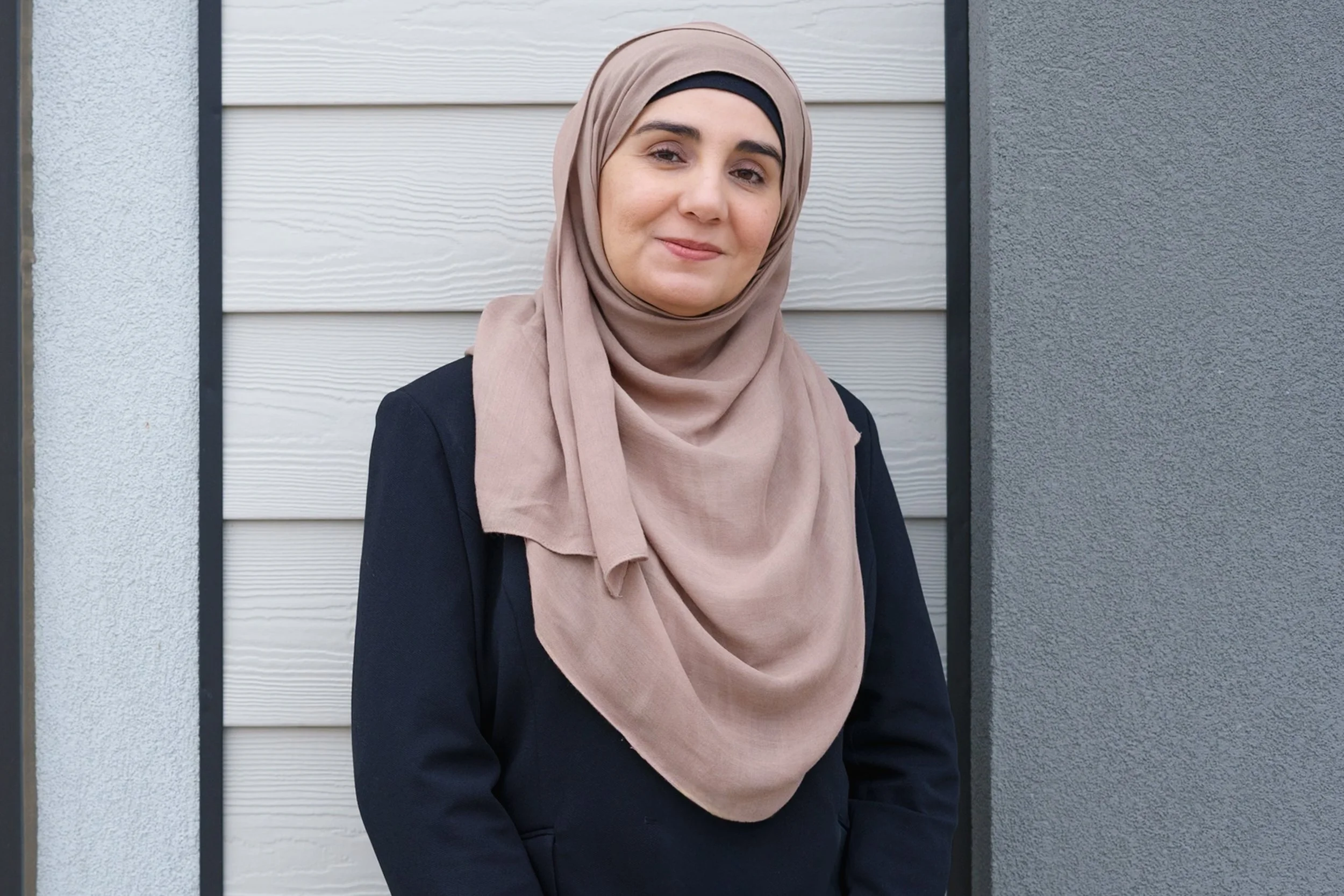 Person holding a round mirror in front of their face, with only part of their head and hand visible, against a plain white wall.