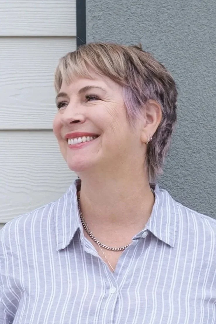 A person holding a round mirror in front of their face, obscuring it from view, while standing against a plain light-colored wall.