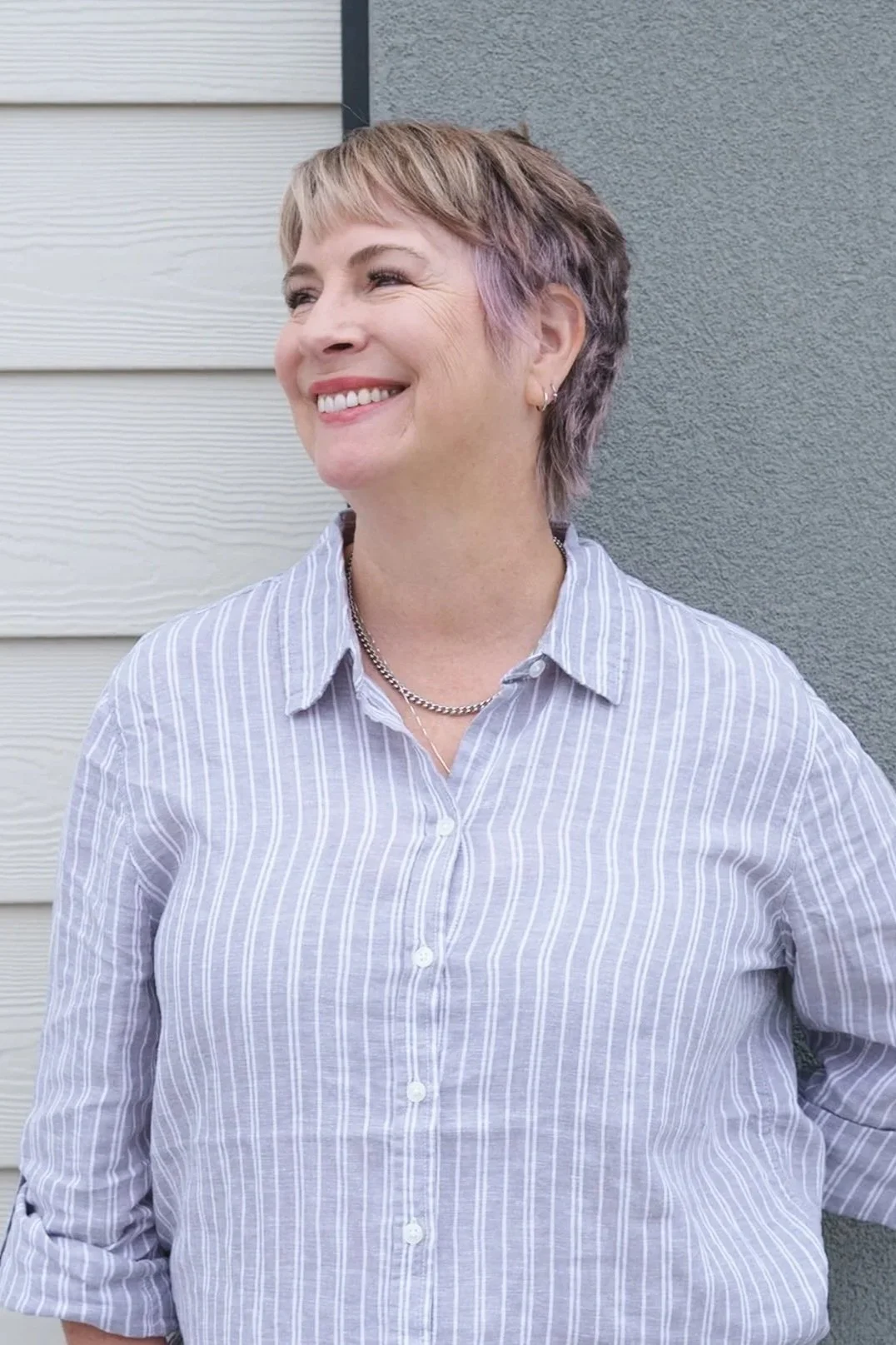 A person holding a round mirror in front of their face, obscuring it from view, while standing against a plain light-colored wall.