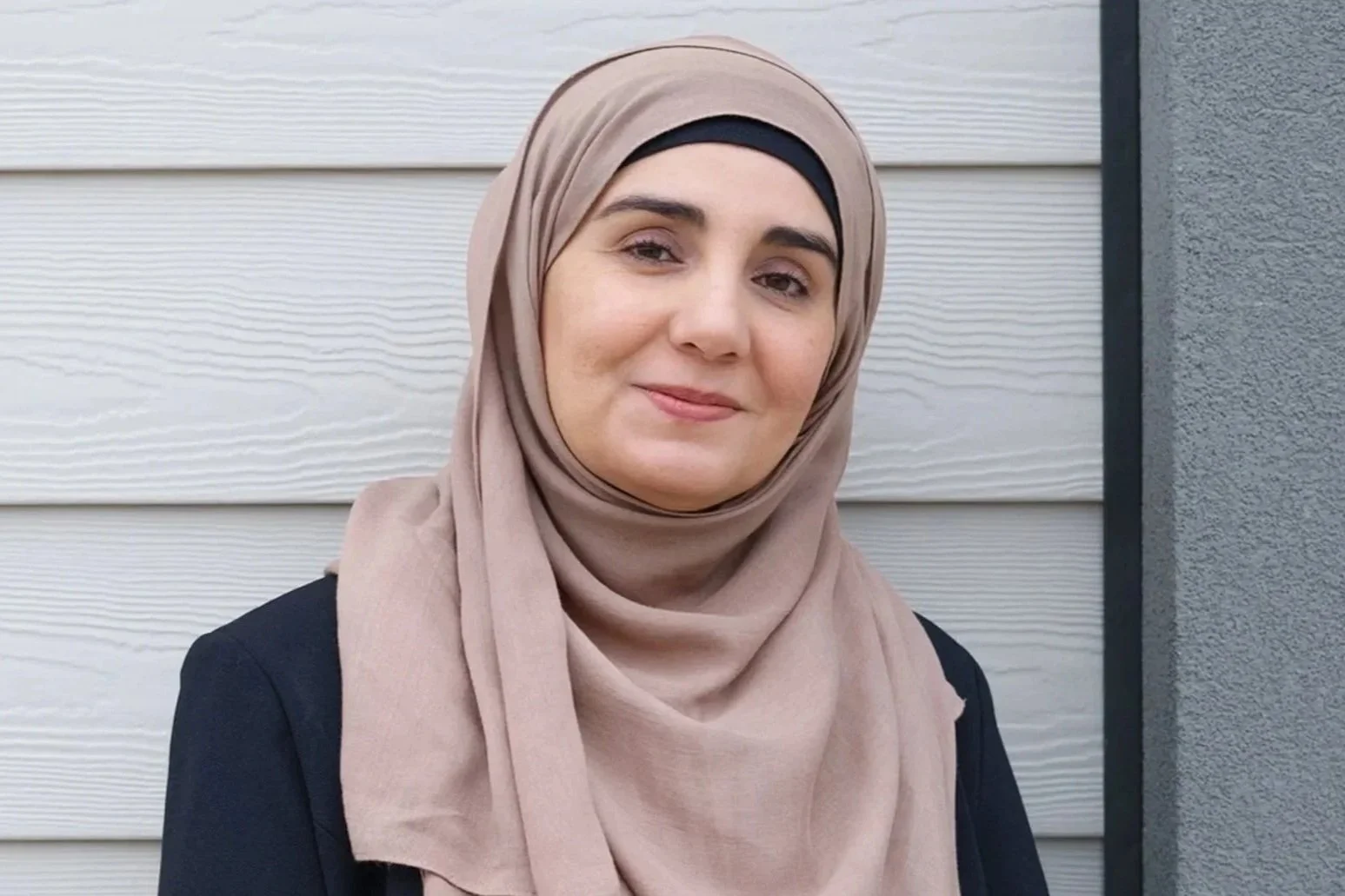 Person holding a round mirror in front of their face, with only part of their head and hand visible, against a plain white wall.