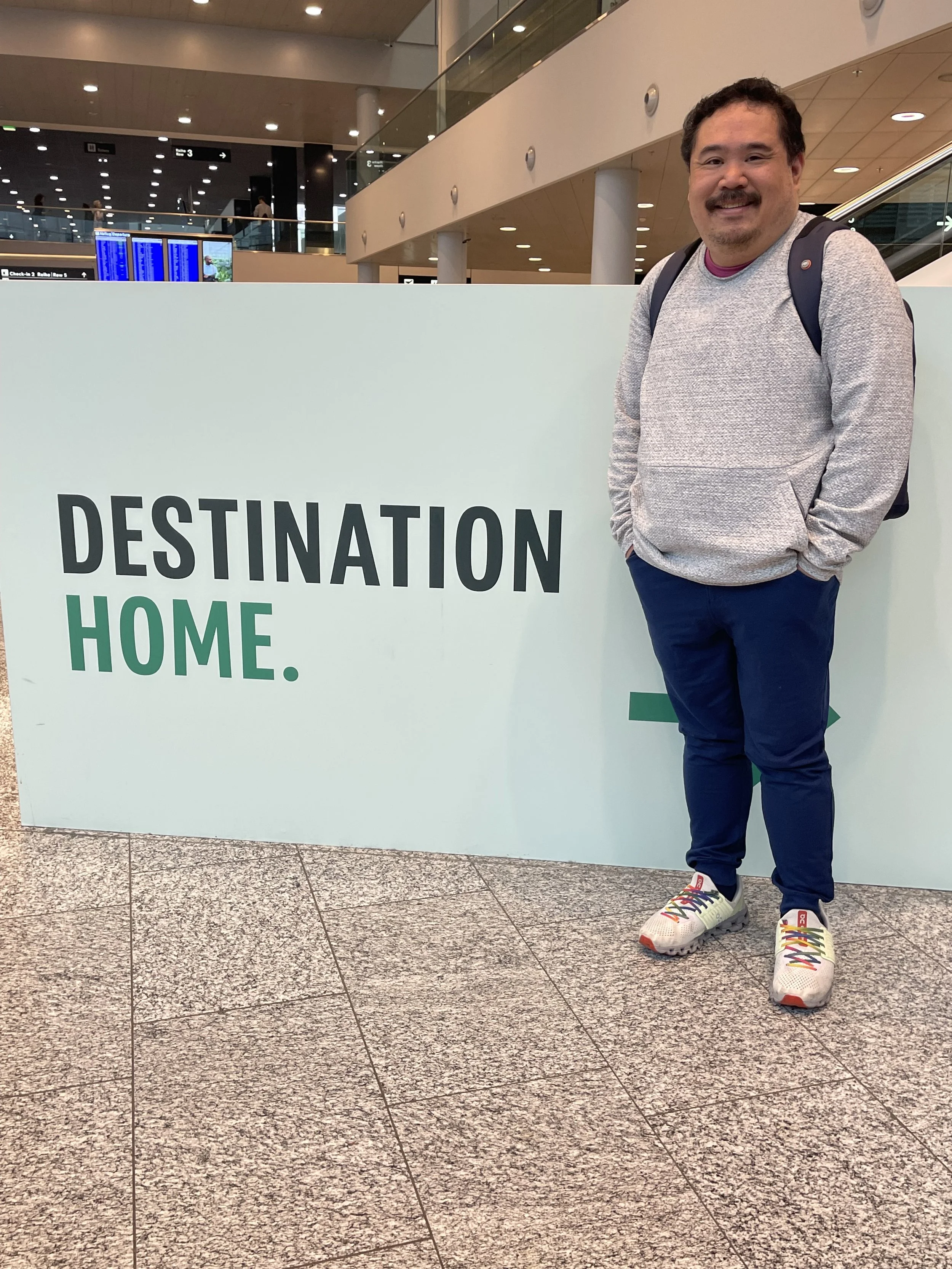 Colin traveling through Zurich Airport in front of a sign that reads 'Destination Home.'