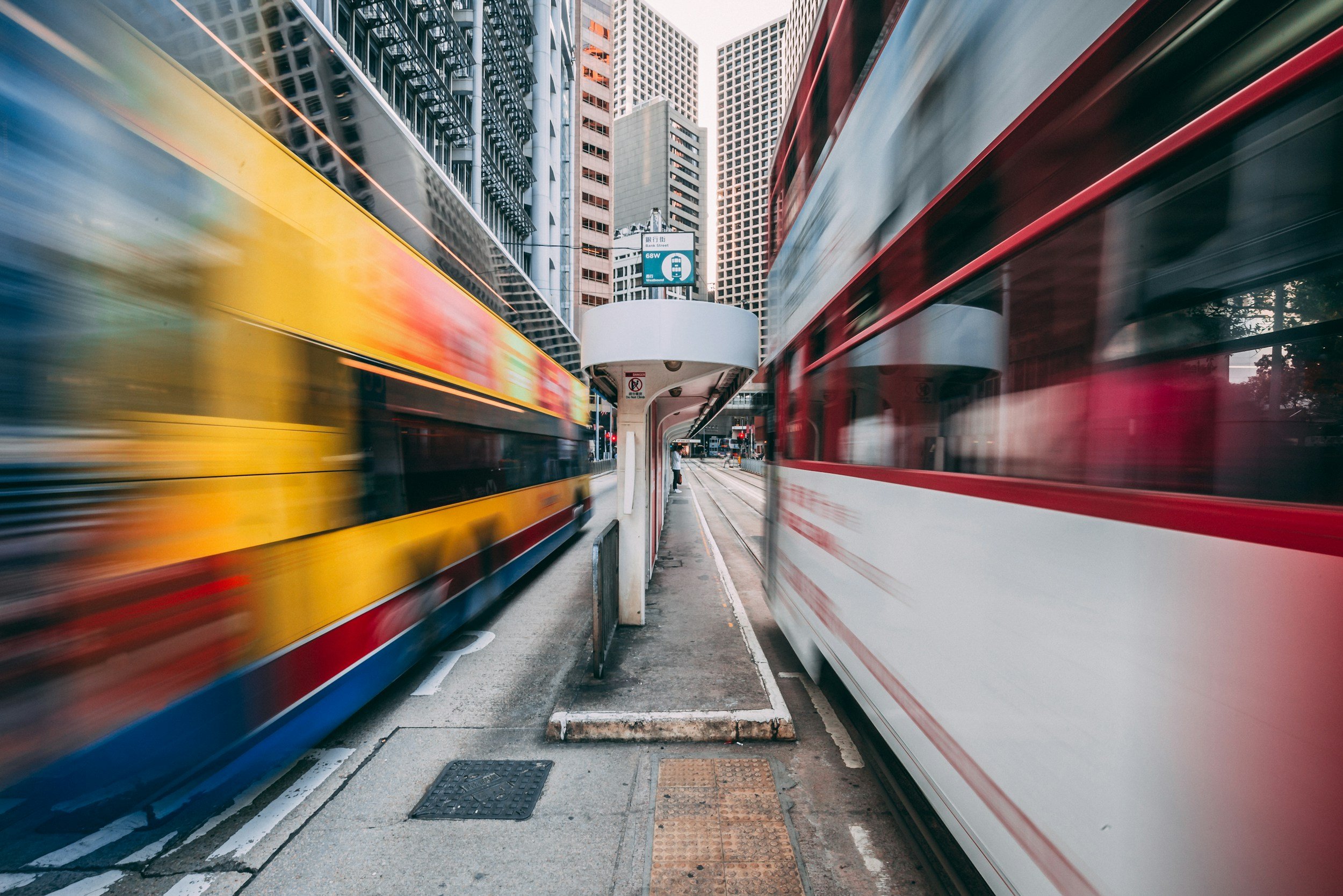 Two double-decker buses traveling in opposite directions on a city street with tall buildings in the background, captured with motion blur.