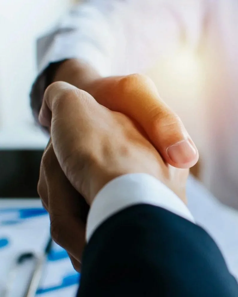 Close-up of two people shaking hands in a professional setting with a blurred background.