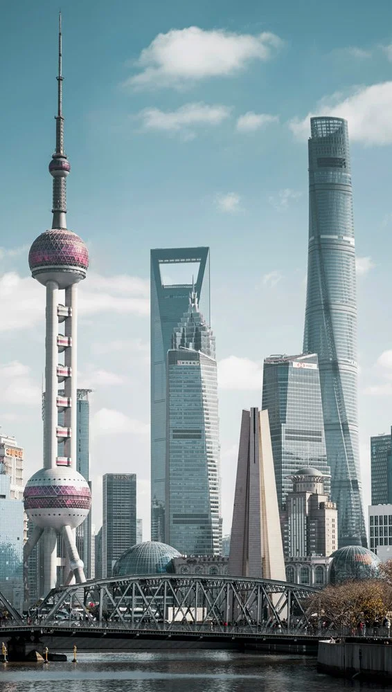 View of Shanghai skyline featuring the Oriental Pearl Tower, Shanghai World Financial Center, Jin Mao Tower, and Shanghai Tower in daytime with a city river in foreground.