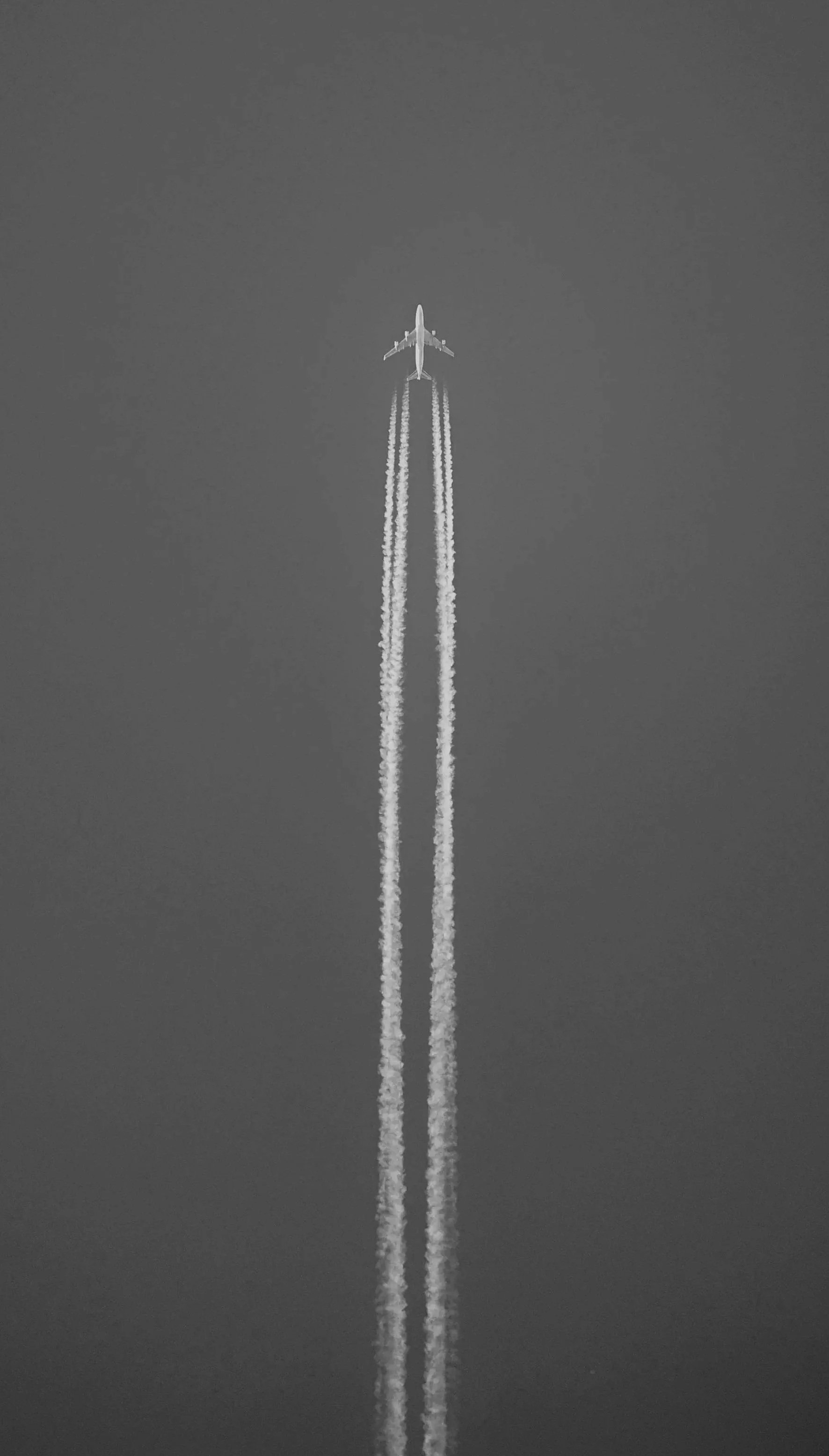 Aerial view of an airplane flying high in the sky with contrails behind it.