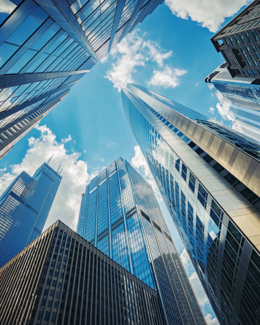 Looking up at tall modern skyscrapers with glass windows against a partly cloudy blue sky.