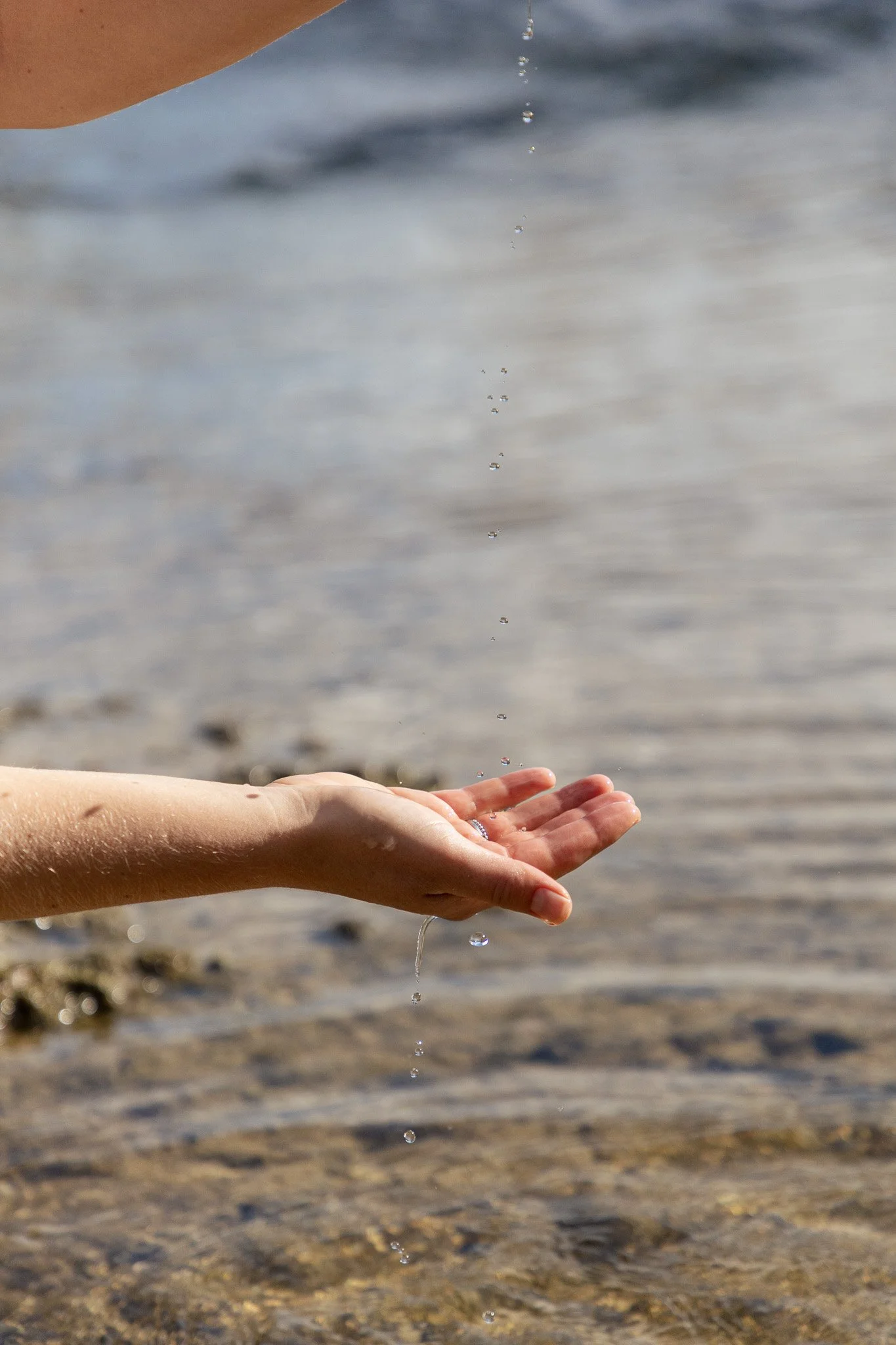 Hände, die Wasser fallen lassen, am Strand