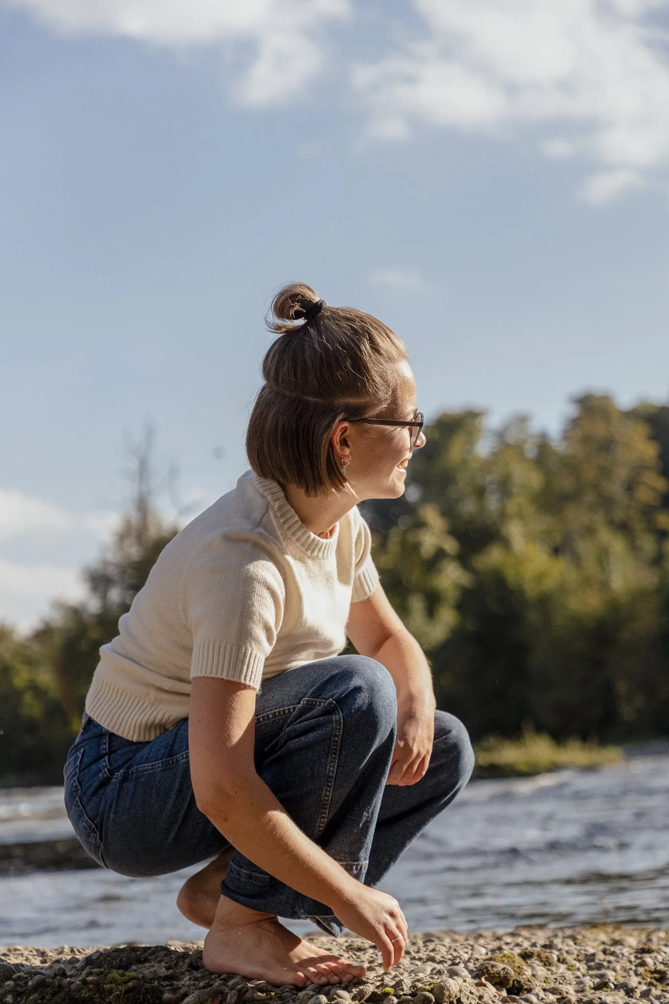 Kristina Lehmann am Flussufer, umgeben von Natur, lächelt ins Sonnenlicht.