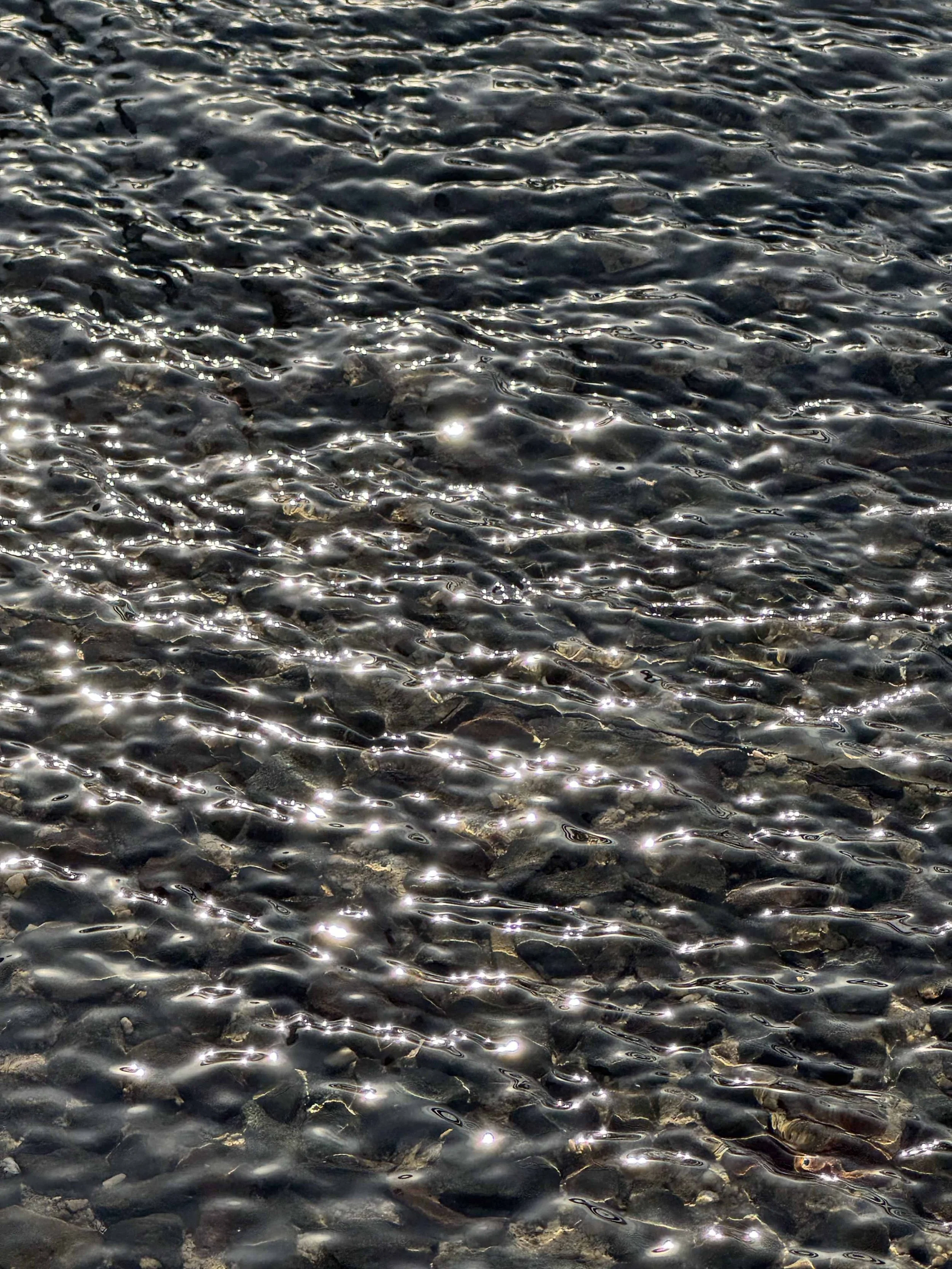 Schatten und Lichtreflexionen auf der Wasseroberfläche mit kleinen Steinen im Wasser.