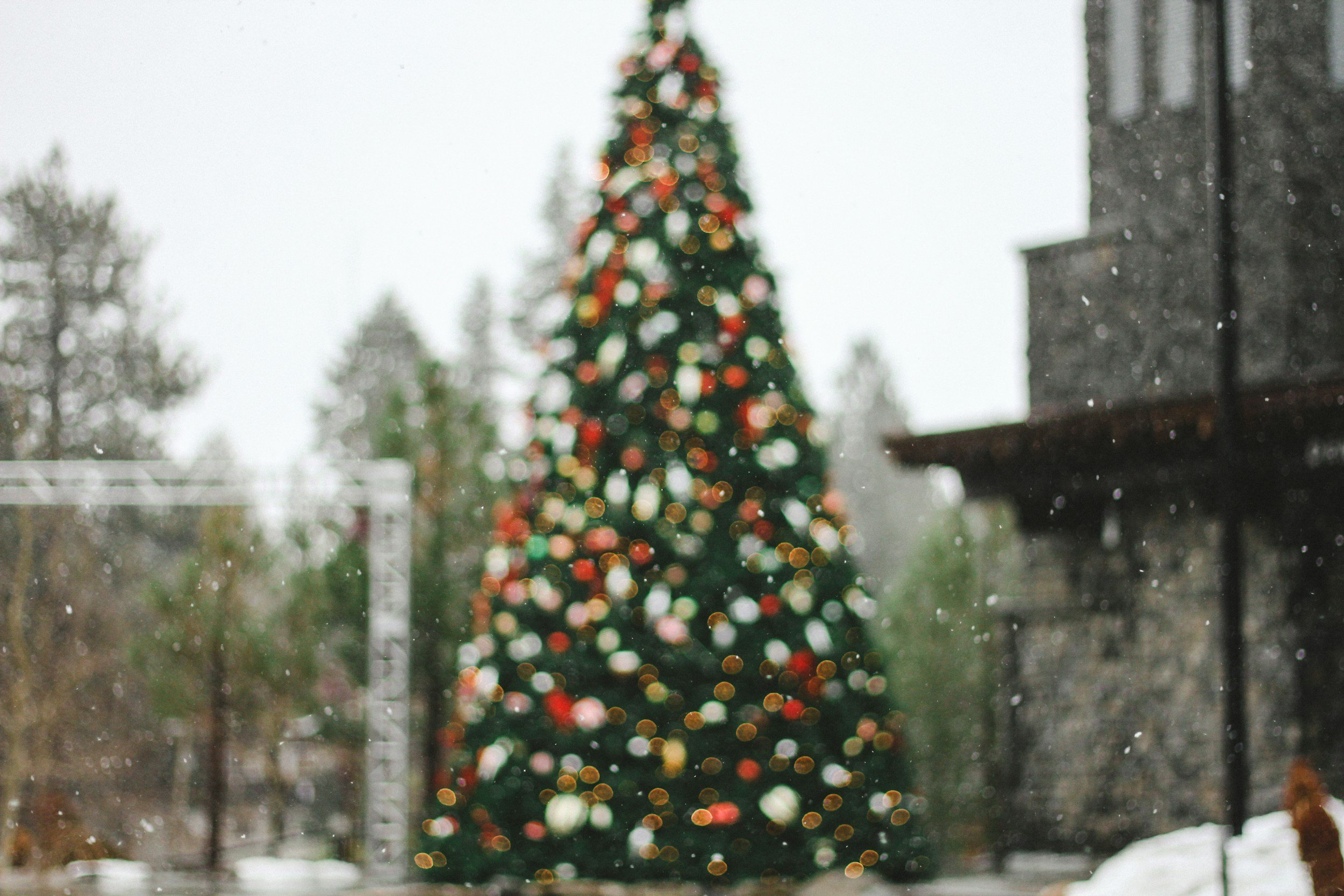 Blurred image of a decorated Christmas tree with colorful lights outside a window on a snowy day.