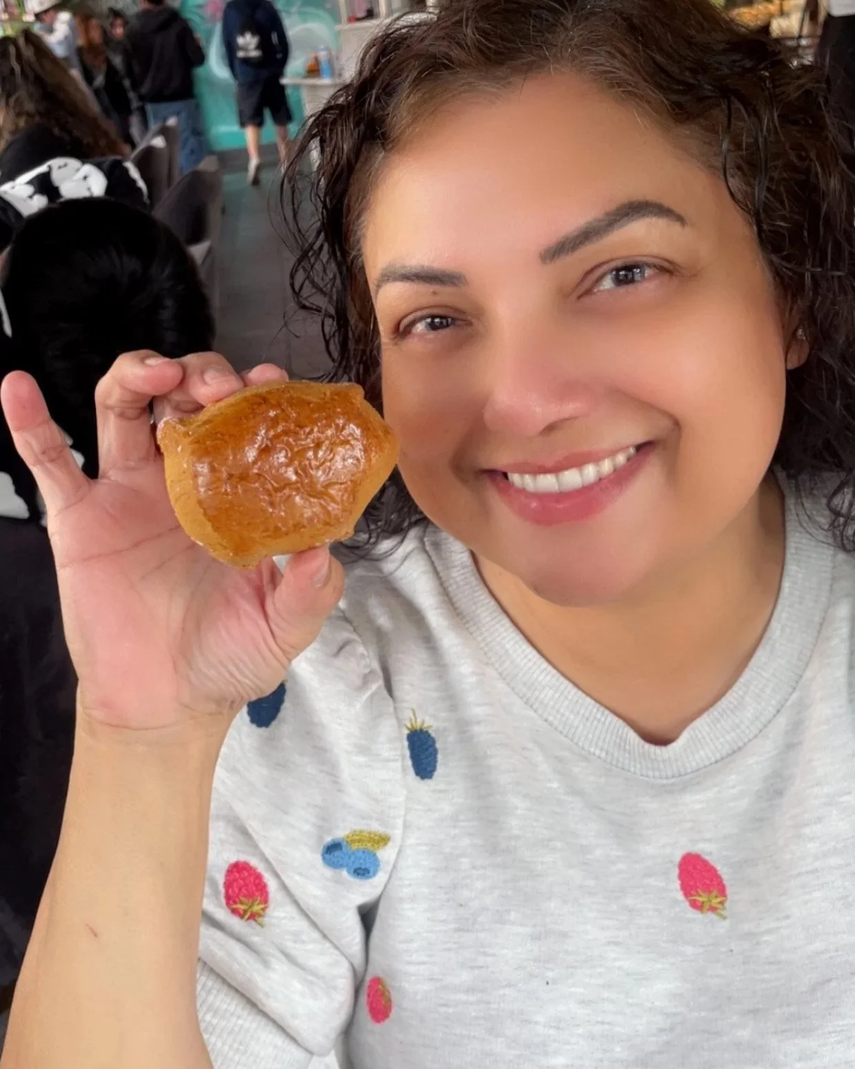 A woman smiling and holding a piece of amber-colored candied ginger in a restaurant or cafe.